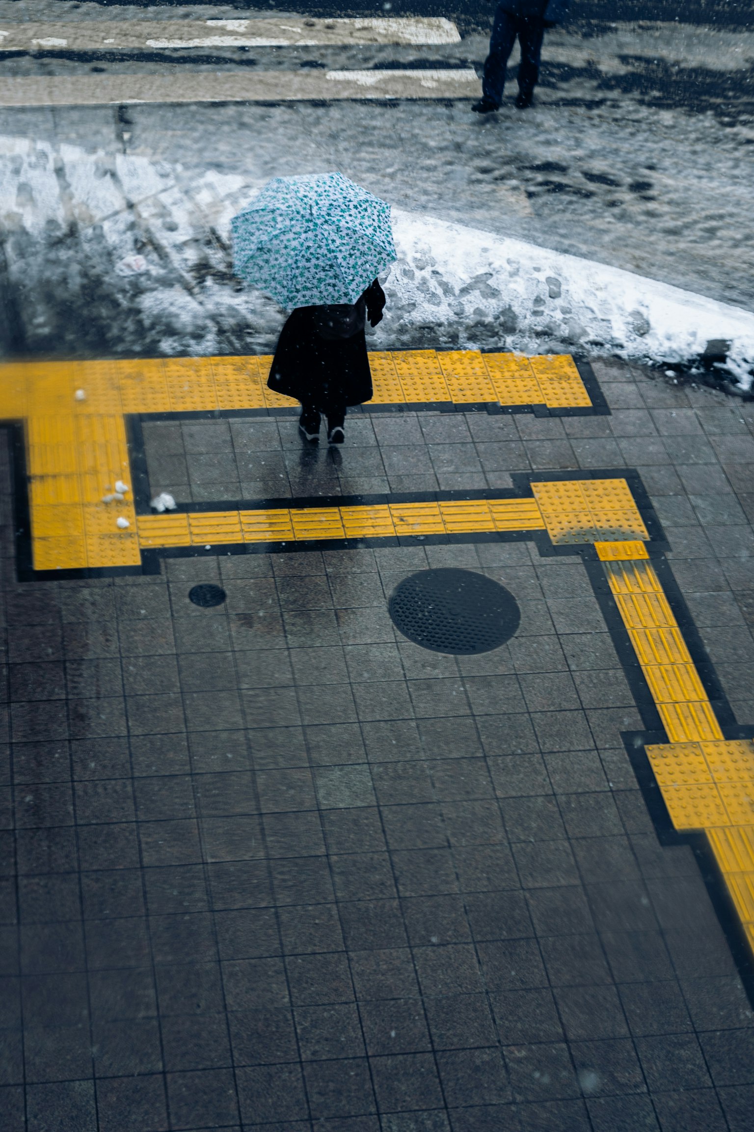 一位拿著藍色雨傘的女士站在有黃色線條的人行道上