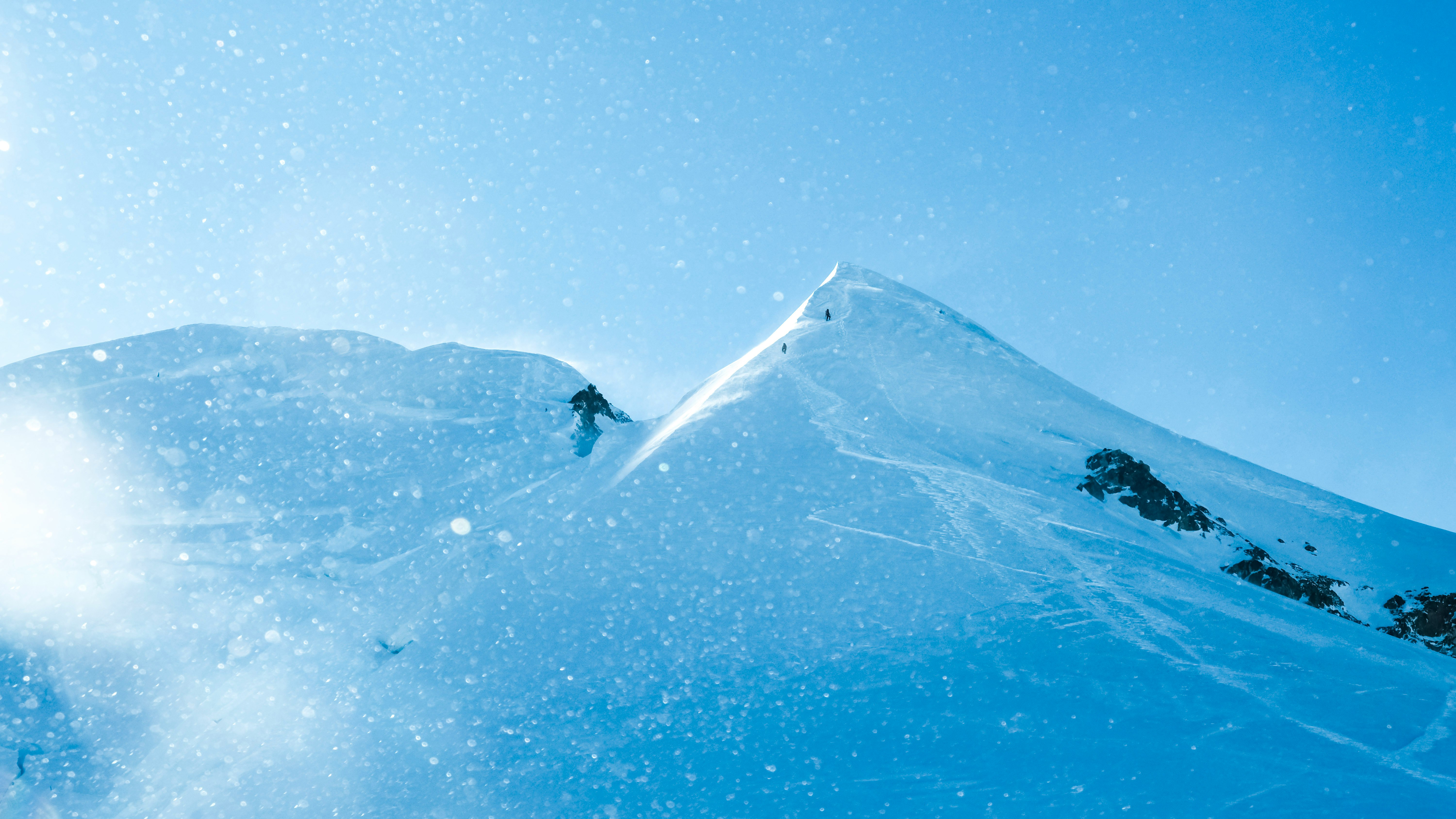 青い空の下で雪煙の中を滑るスキーヤーのある山の斜面