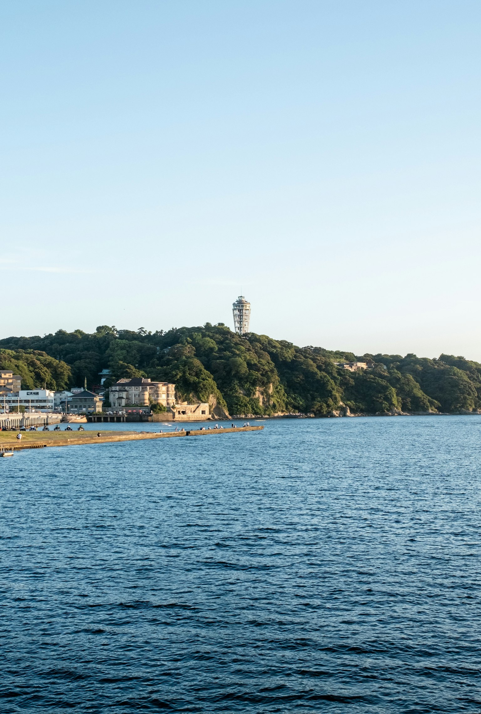 Vue panoramique de la mer calme avec une colline verte et un phare