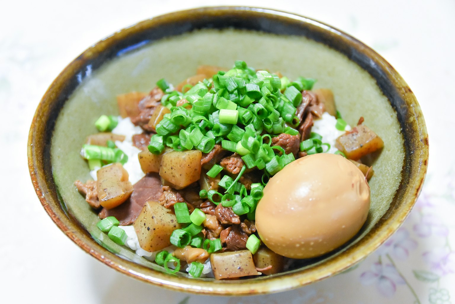 ข้าวในชามที่มีเนื้อเปื่อยและหัวไชเท้าประดับด้วยต้นหอมข้างๆ ไข่ต้ม