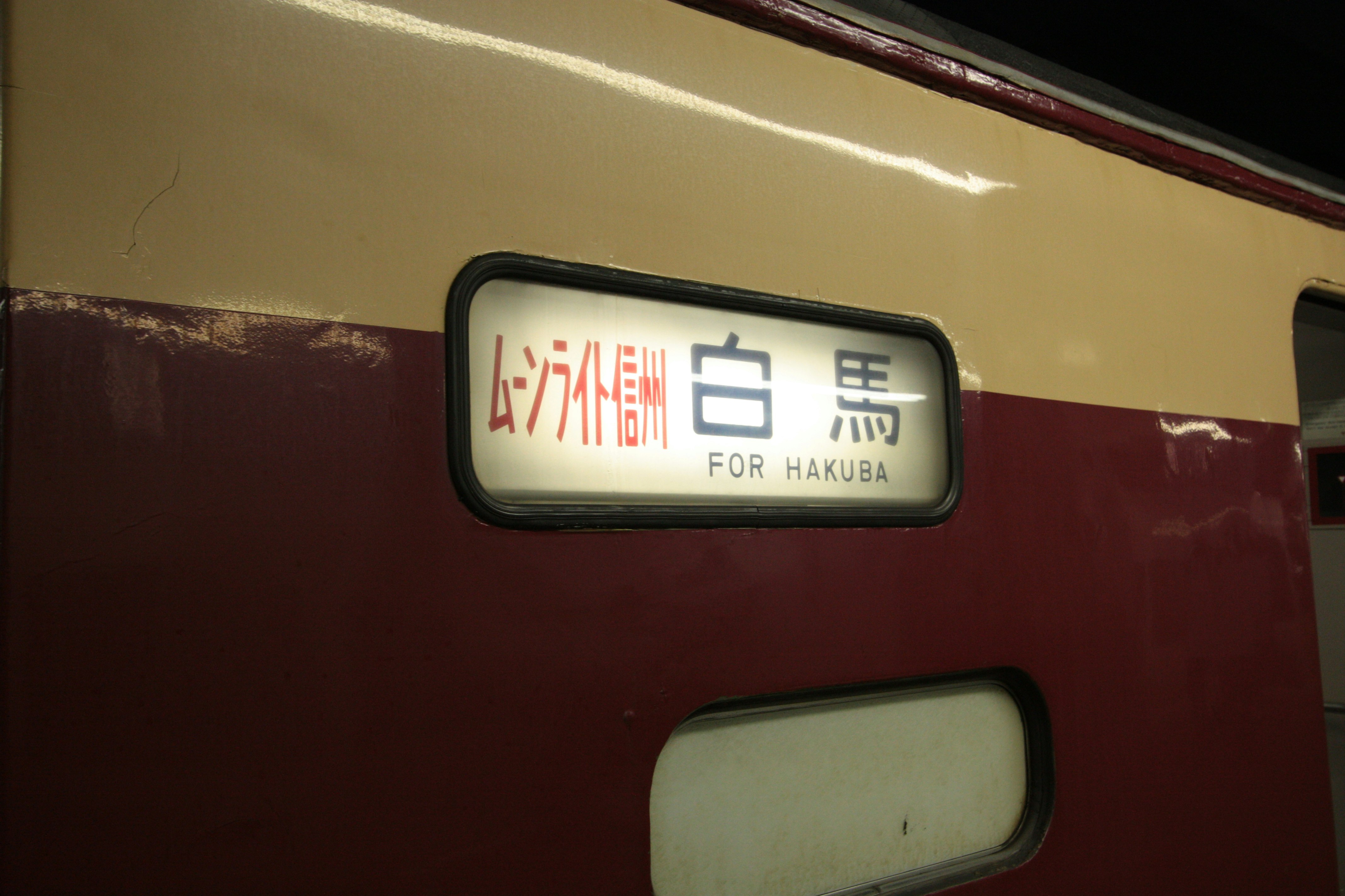 side of a train with station signage and a “FOR HAKUBA” plate