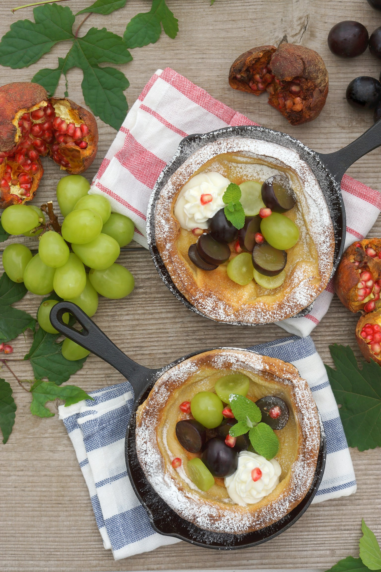 Dos sartenes con postre de frutas y crema rodeadas de uvas y granada