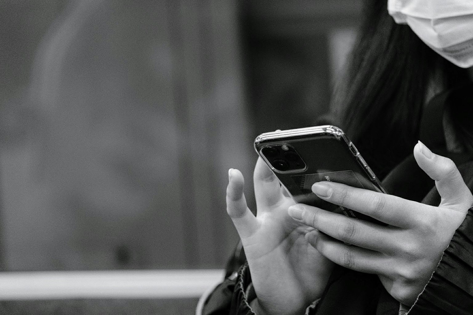 Una persona con una maschera che usa uno smartphone in un'immagine in bianco e nero