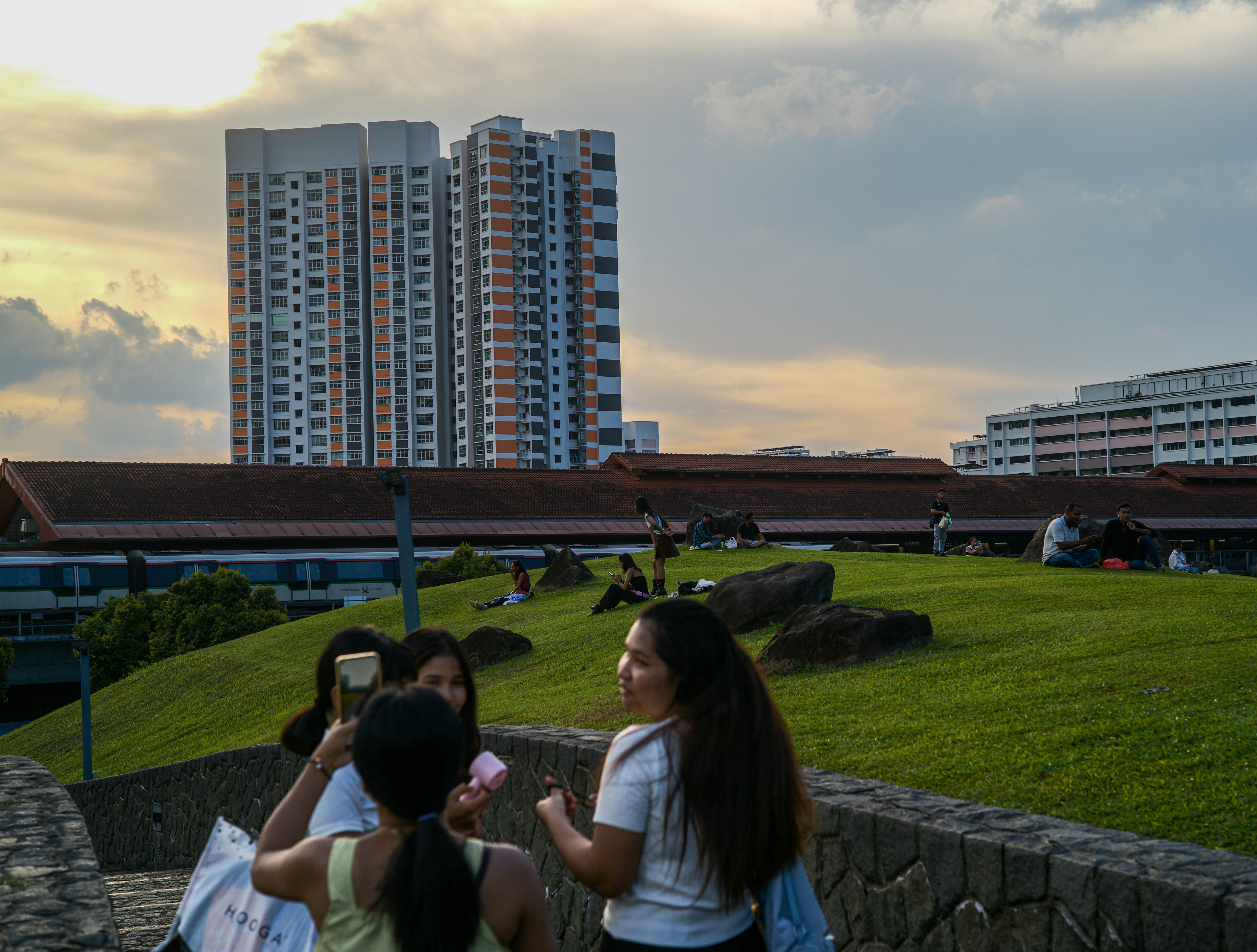 芝生の公園でスマホを撮る人々と高層住宅のある夕景