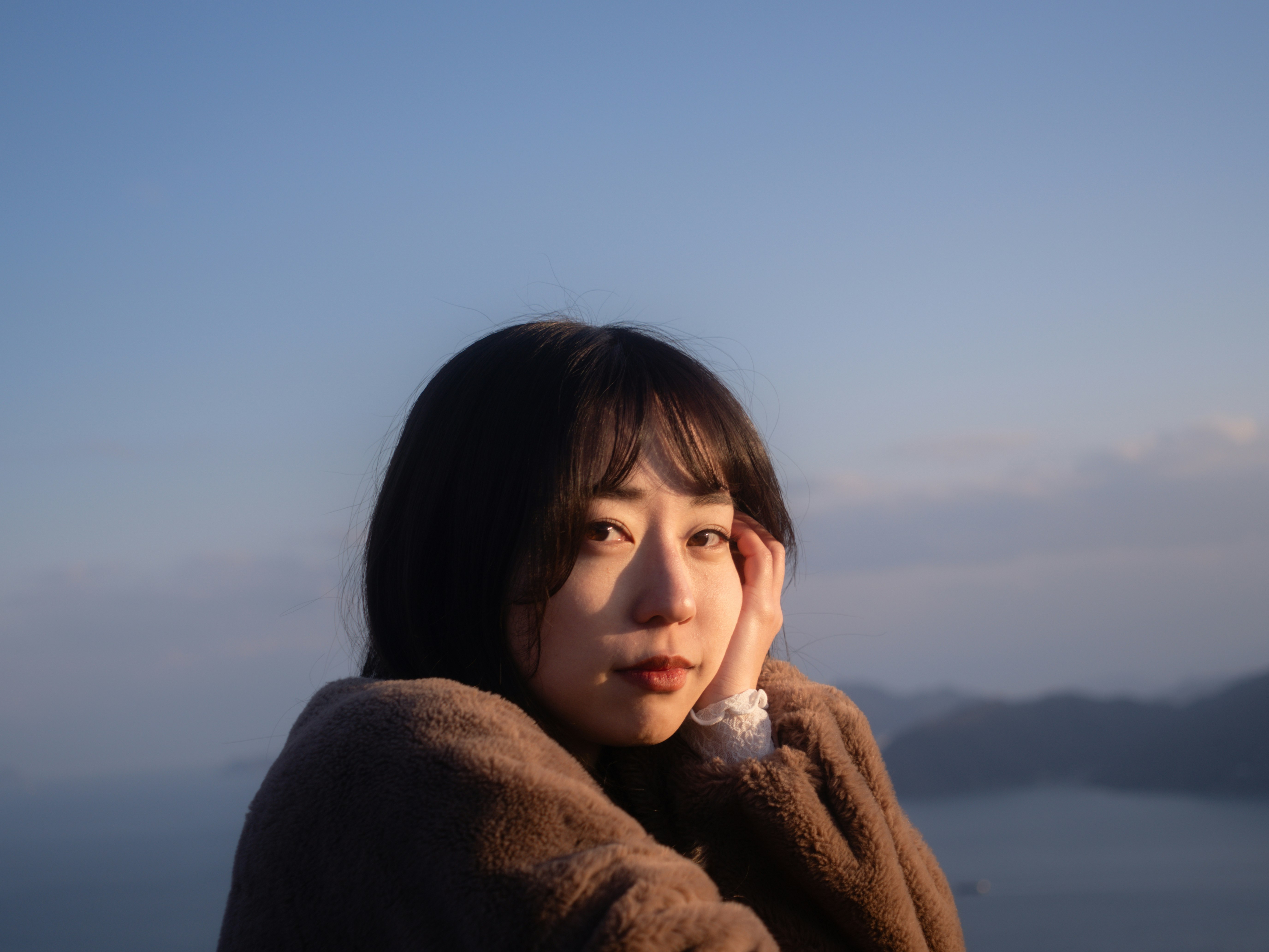 海を望む夕暮れの屋外で頬杖をつく女性
