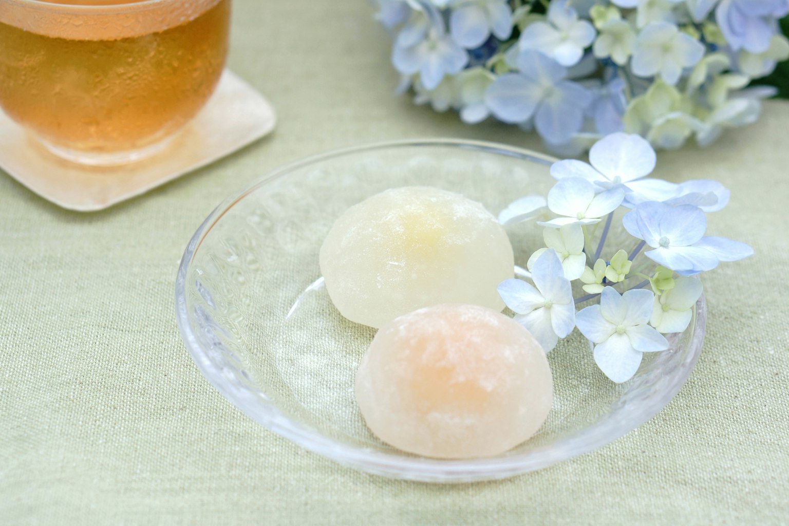 Dua kue Jepang di atas piring transparan di samping bunga biru dan minuman