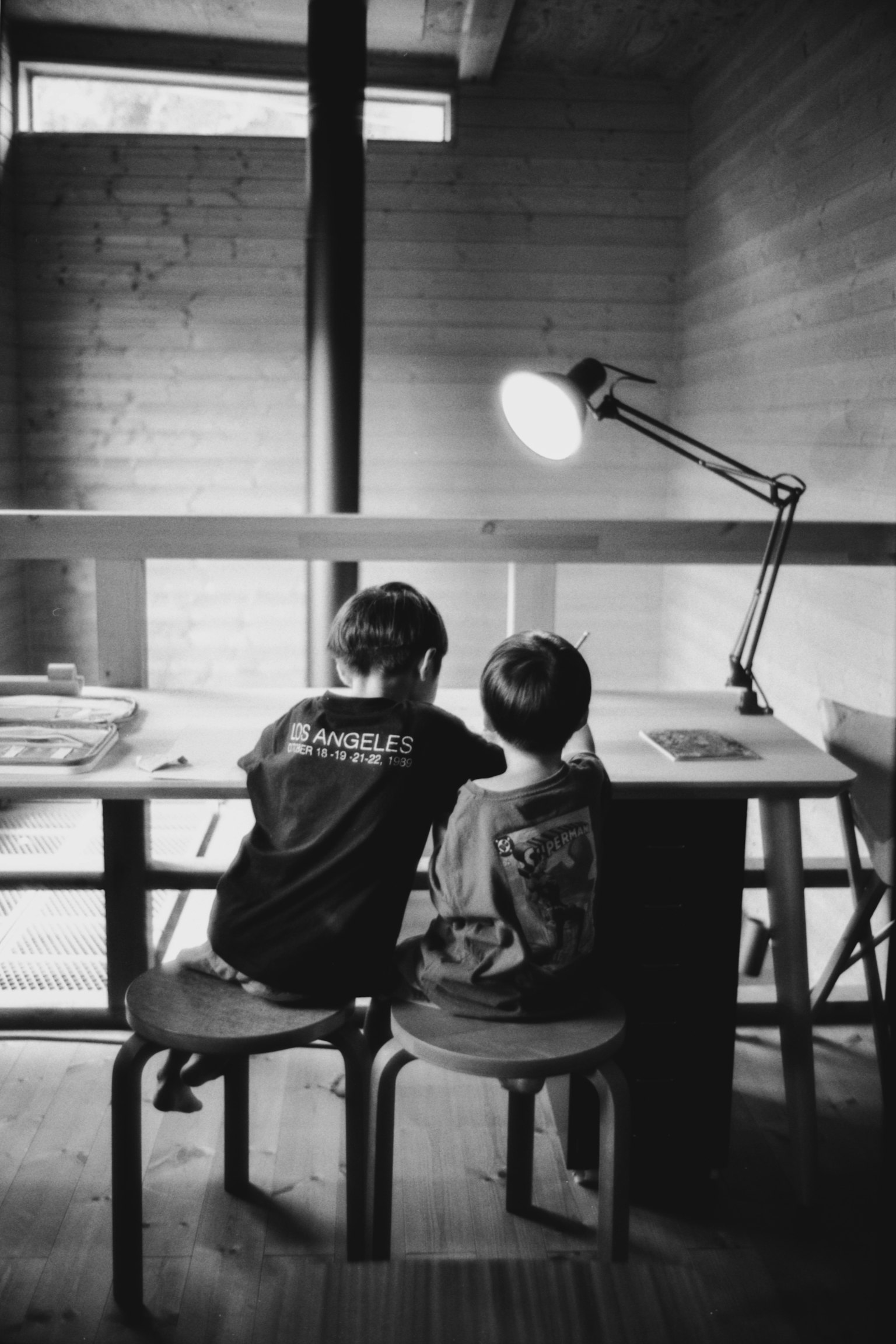 Deux enfants assis à un bureau dans une photo en noir et blanc Chambre lumineuse avec une lampe illuminant leur moment calme