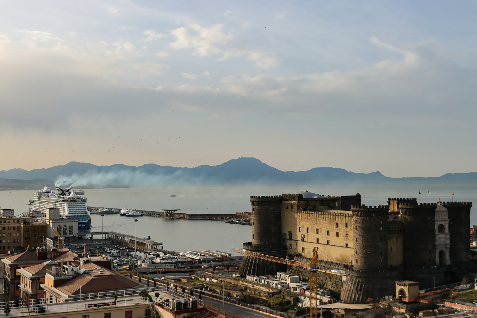 Vista costera de Nápoles con una fortaleza un puerto y montañas a lo lejos