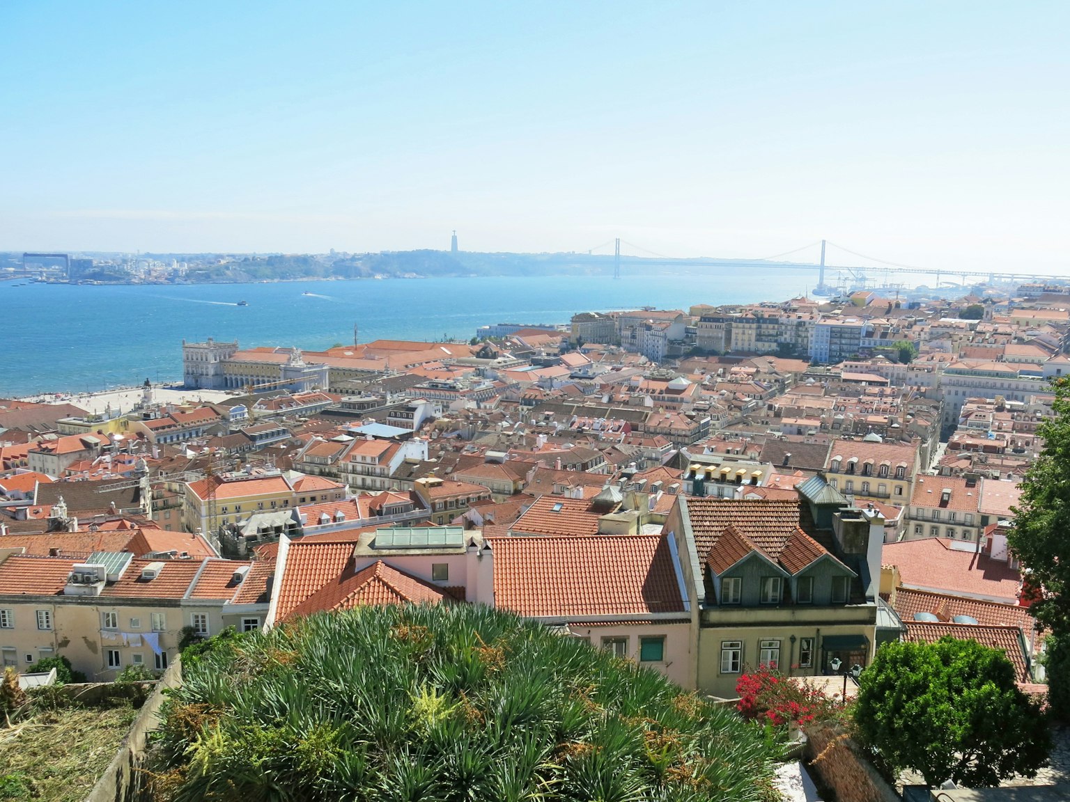 A panoramic view of Lisbon featuring red-roofed buildings and blue ocean