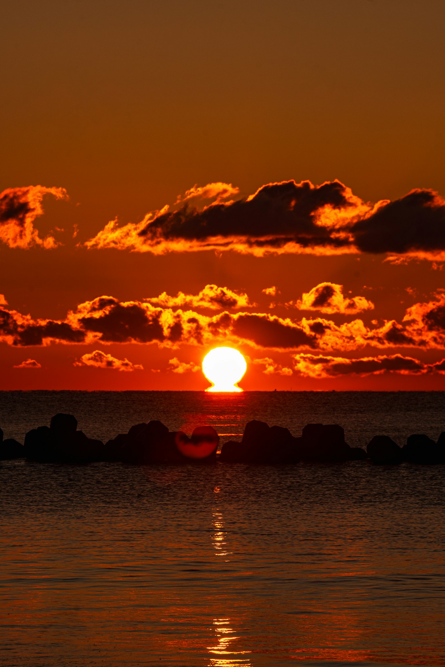 Schöner Sonnenuntergang über dem Ozean mit orangefarbenem Himmel und Wolkenreflexionen