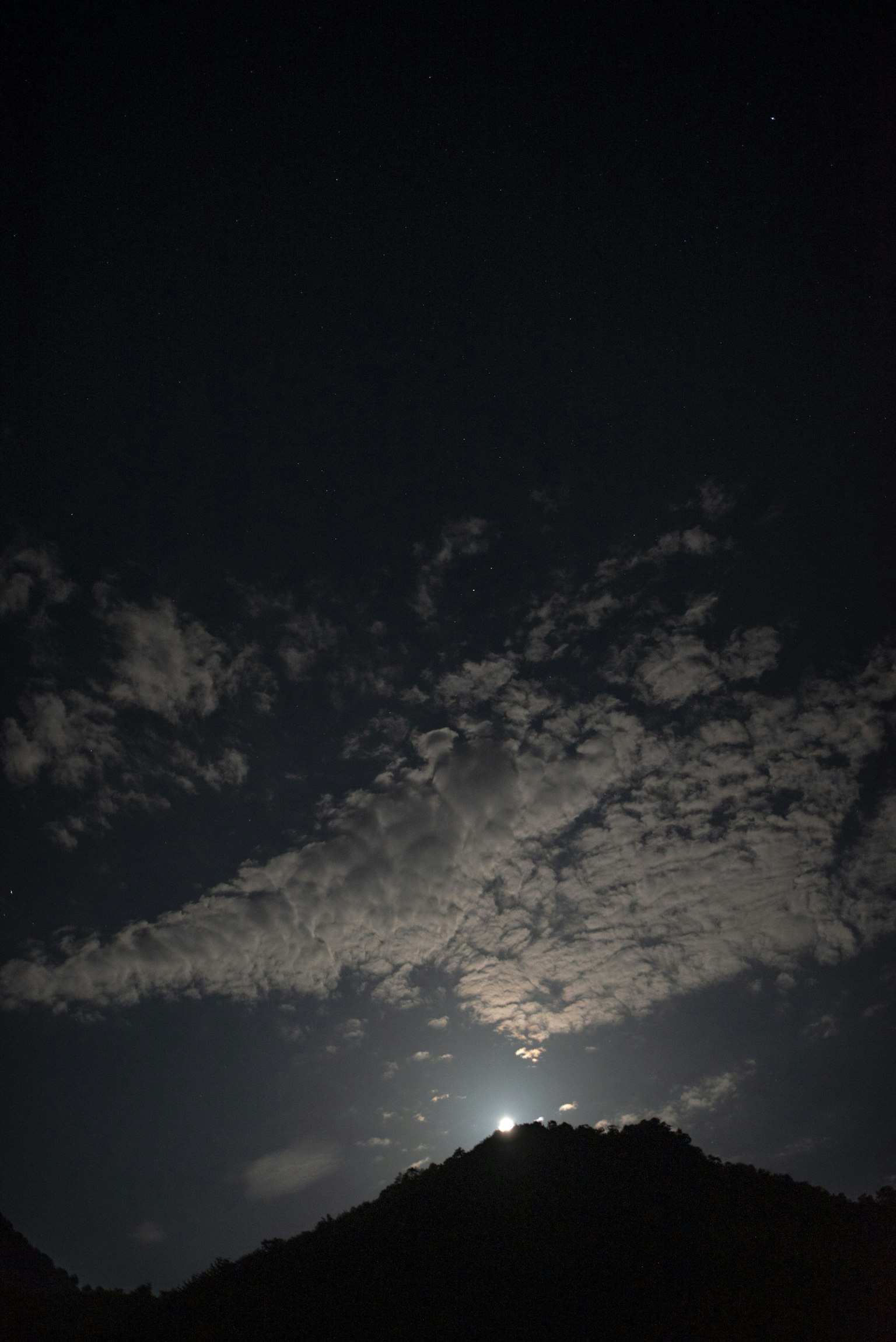 Luna che illumina le nuvole sopra il profilo di una montagna di notte