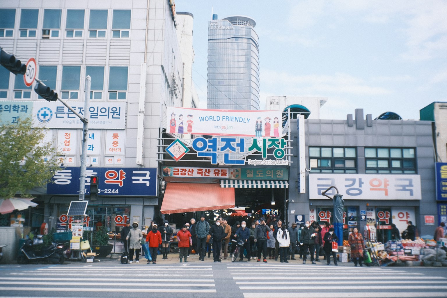 Crowd gathered at the entrance of a traditional market with skyscrapers in the background