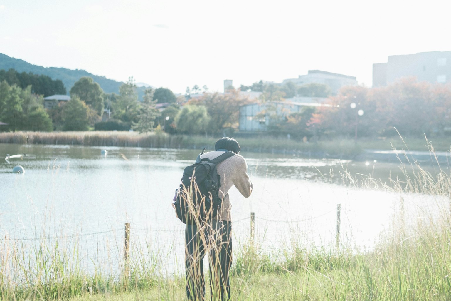 Silhouette di un uomo con una macchina fotografica vicino a un lago con montagne e edifici sullo sfondo