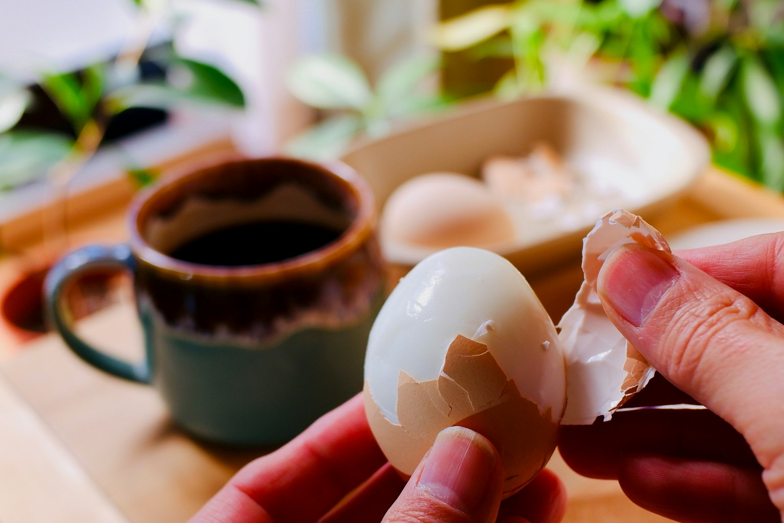 Tangan mengupas cangkang telur dengan cangkir kopi di atas meja