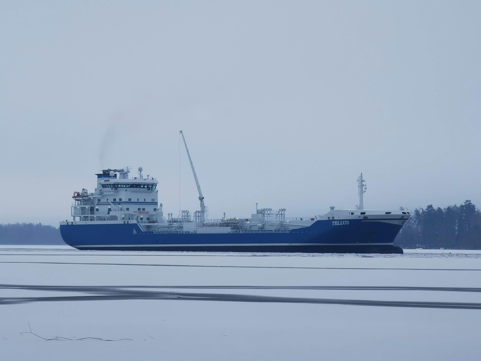 Kapal kargo biru berlayar di atas es dengan pemandangan bersalju