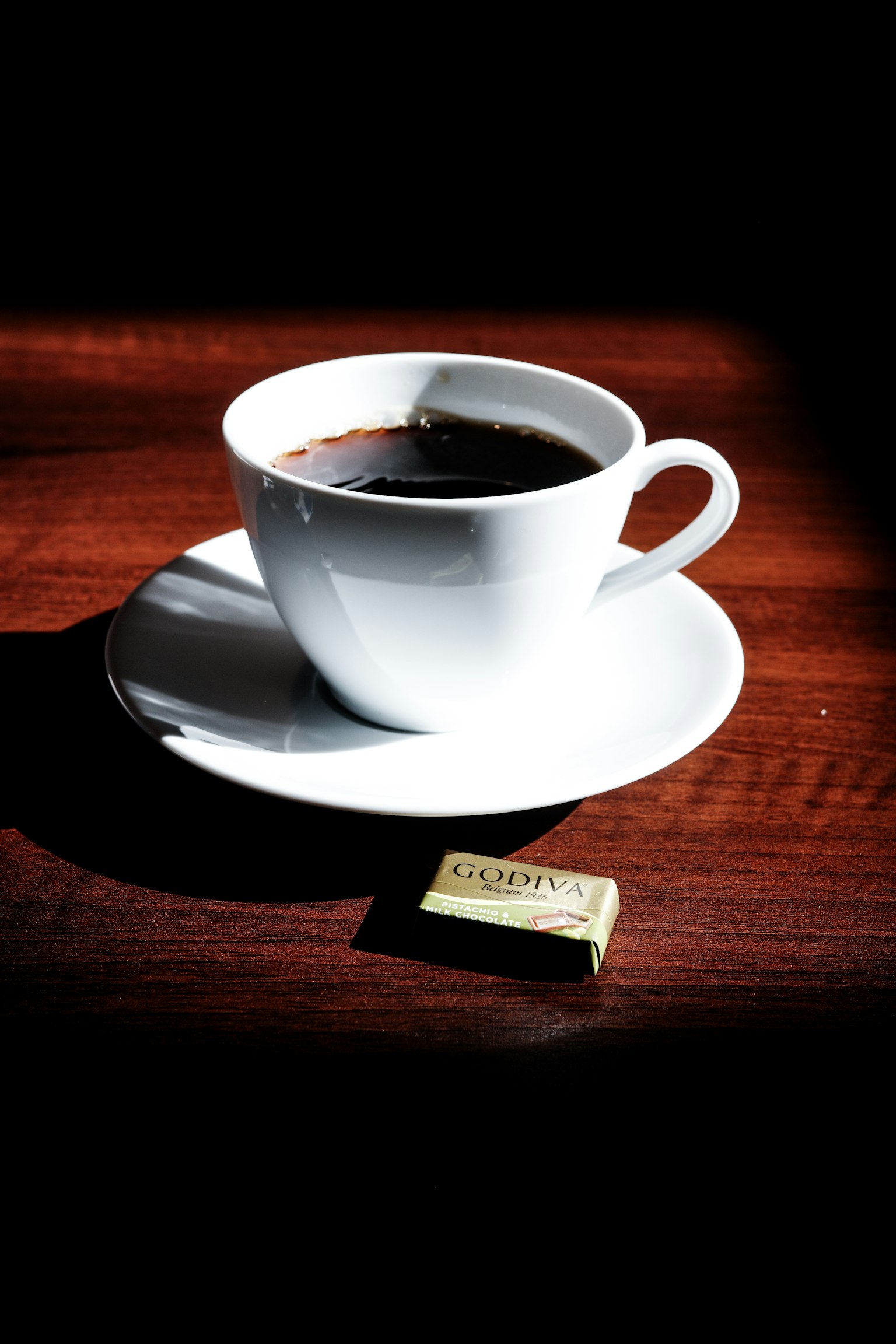 Tasse de café blanche avec soucoupe remplie de café et un morceau de chocolat