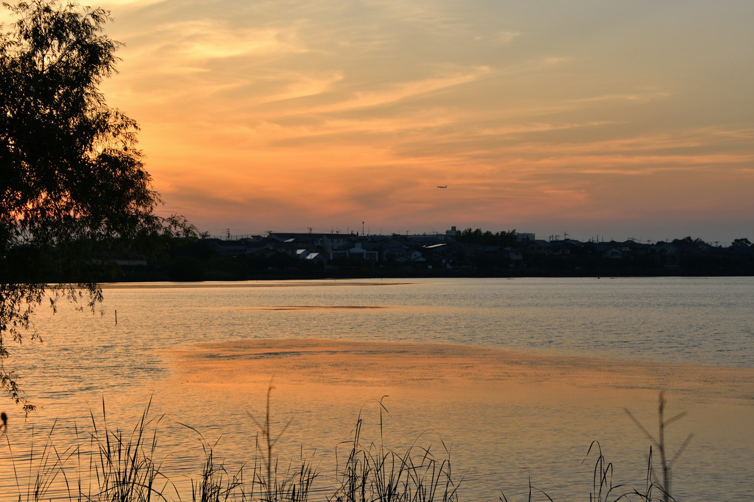 Atardecer sobre un lago tranquilo, reflejos en el agua, tonos naranjas y rosados en el cielo