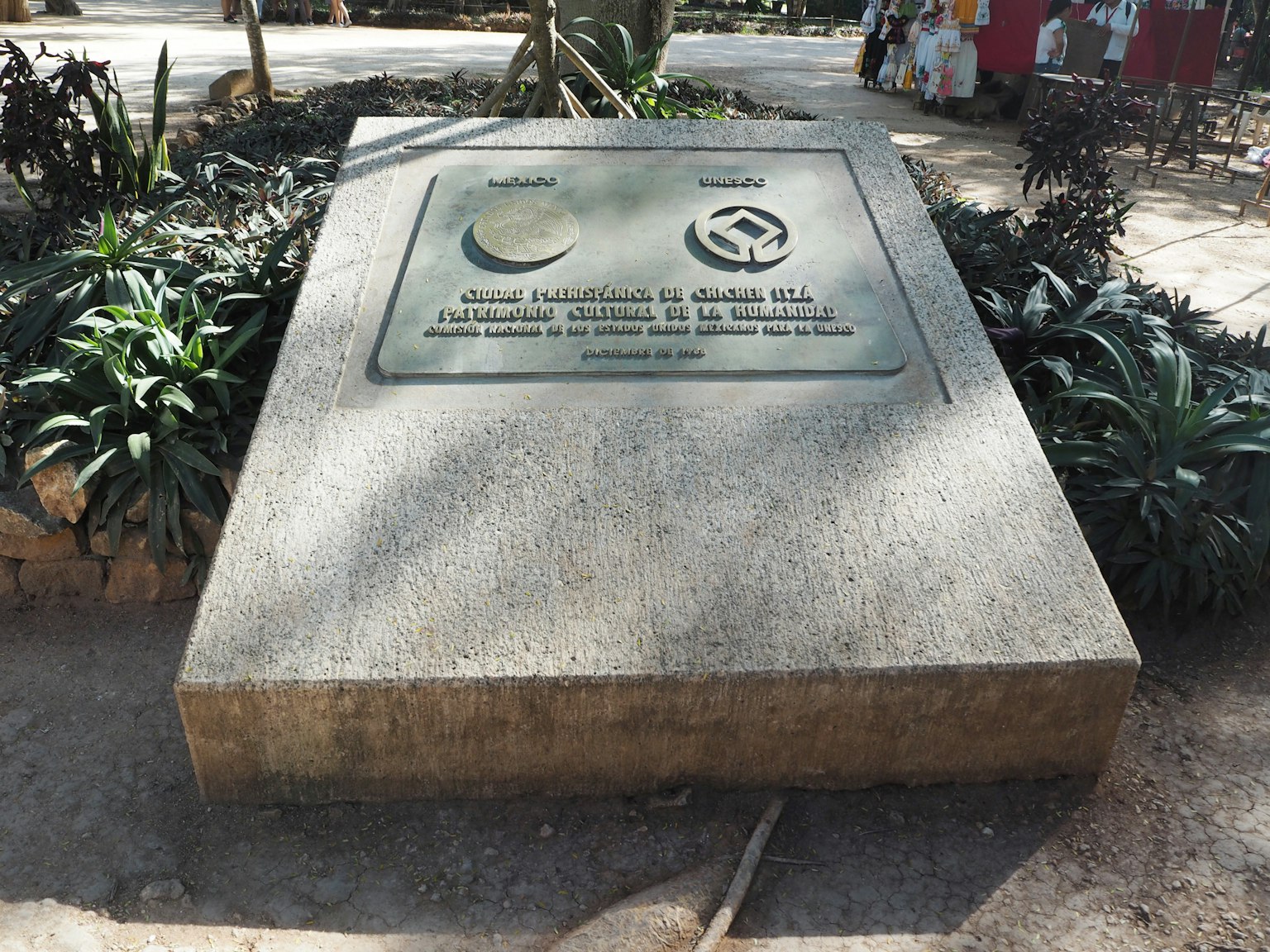 Un monumento de piedra en un parque con una placa conmemorativa rodeada de plantas