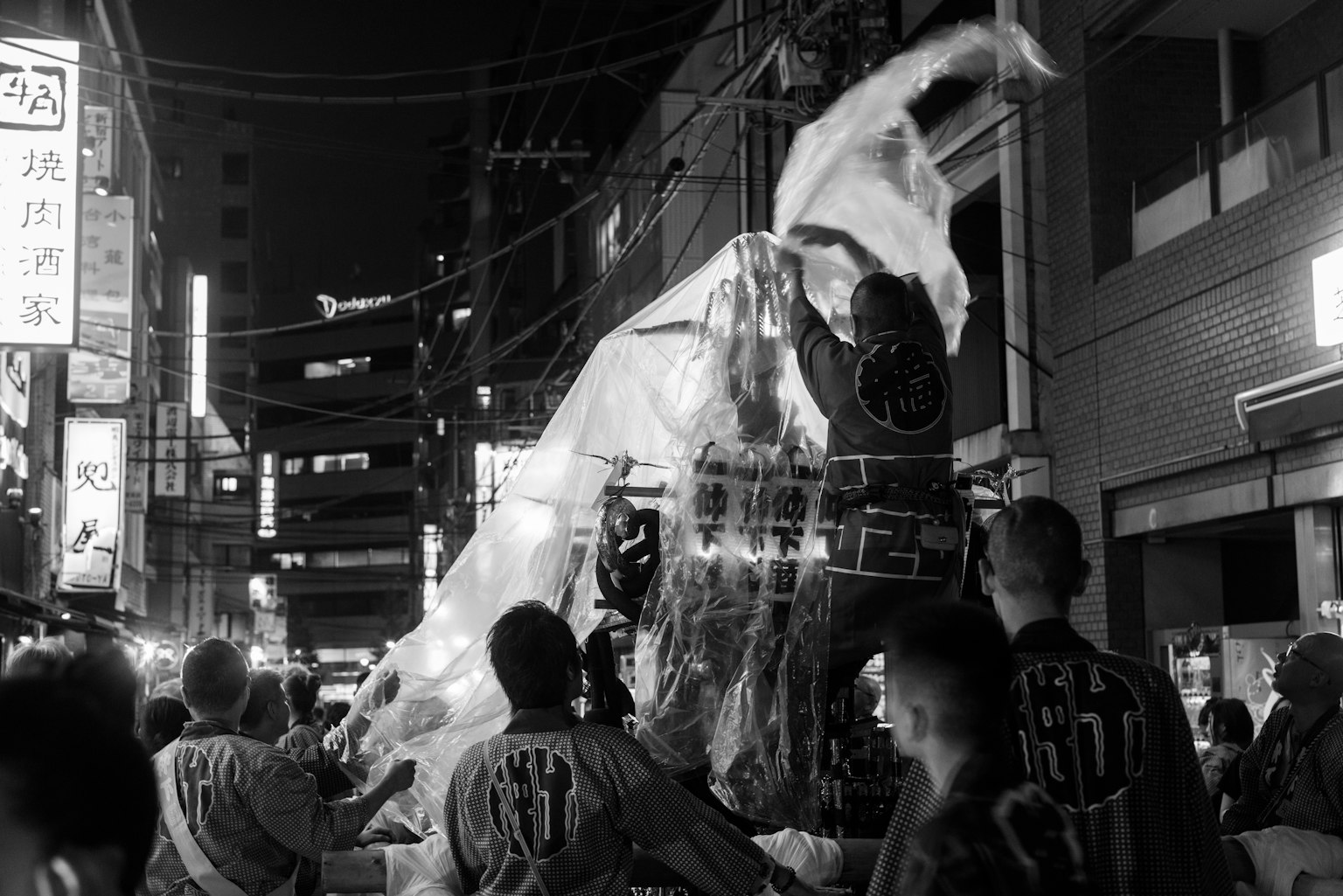 Black and white photo of people carrying a mikoshi during a night festival