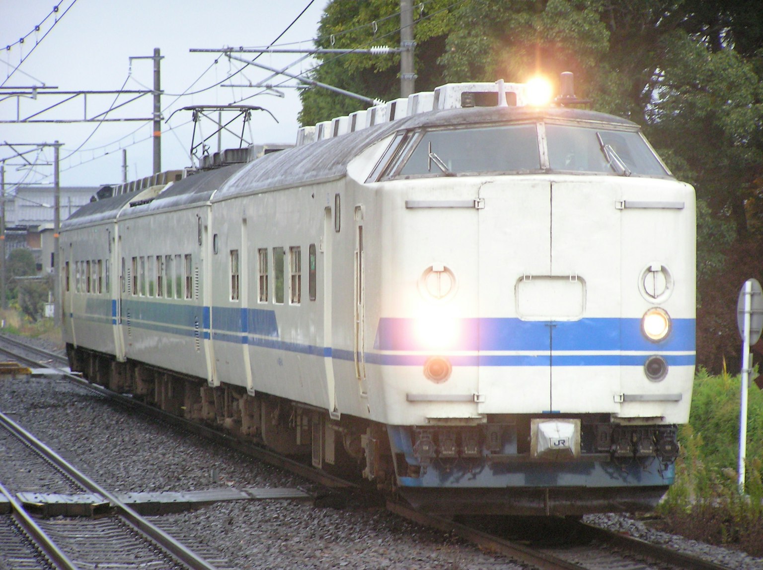White train with blue stripes traveling in the rain