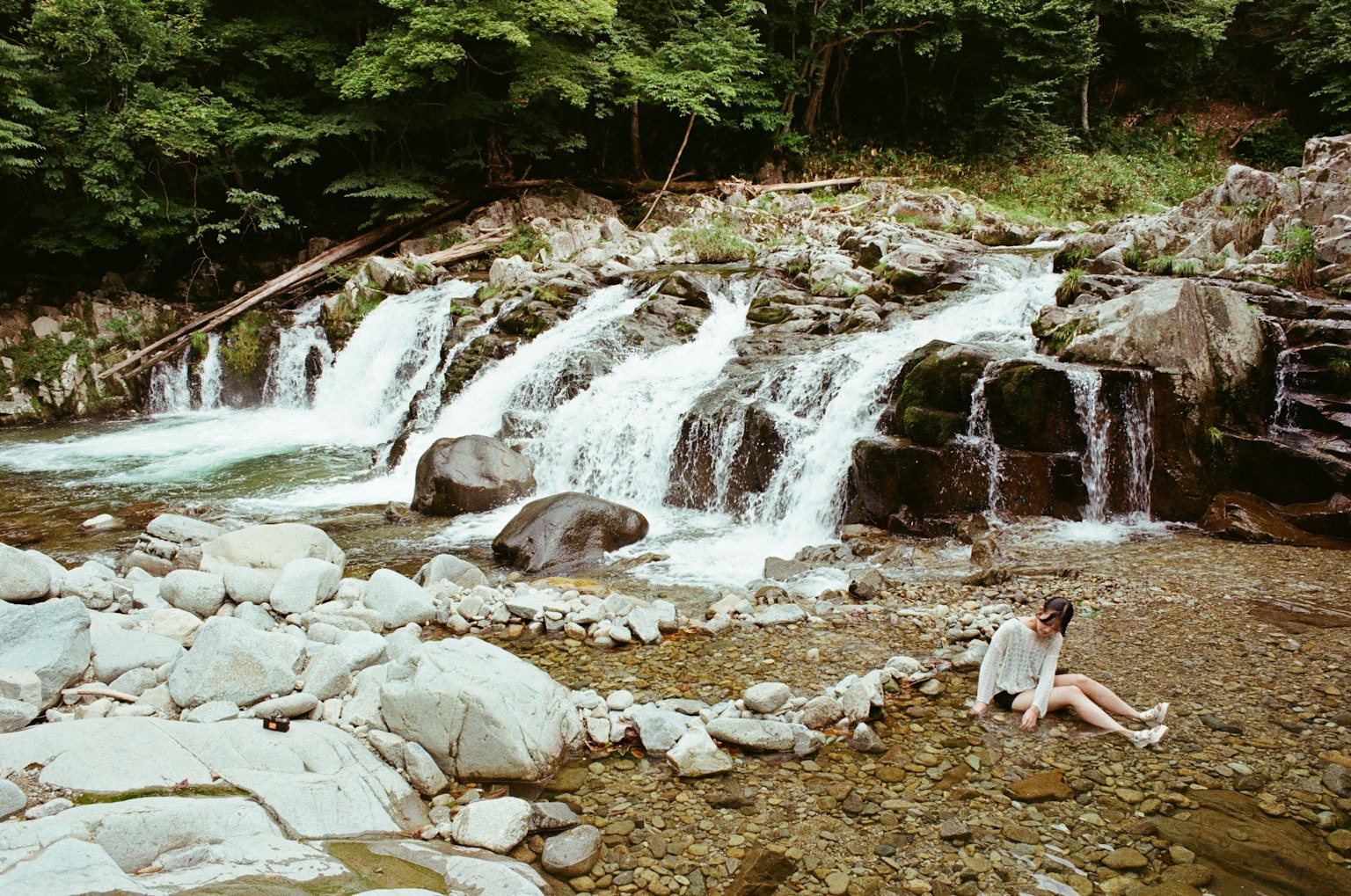 小さな滝が流れる川のそばに座っている女性の姿 緑豊かな木々に囲まれた自然の風景