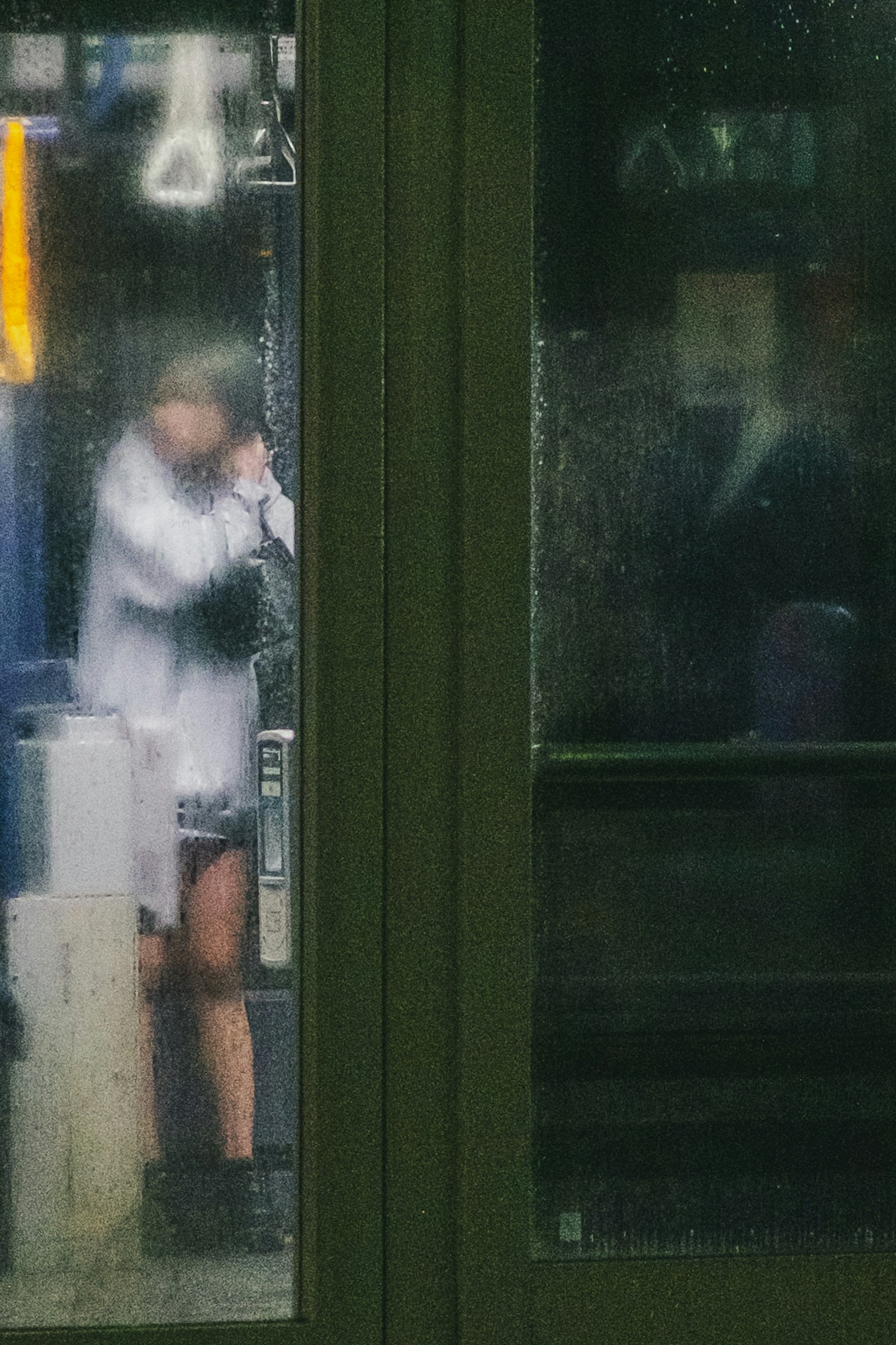 A person making a phone call at a bus stop in the rain