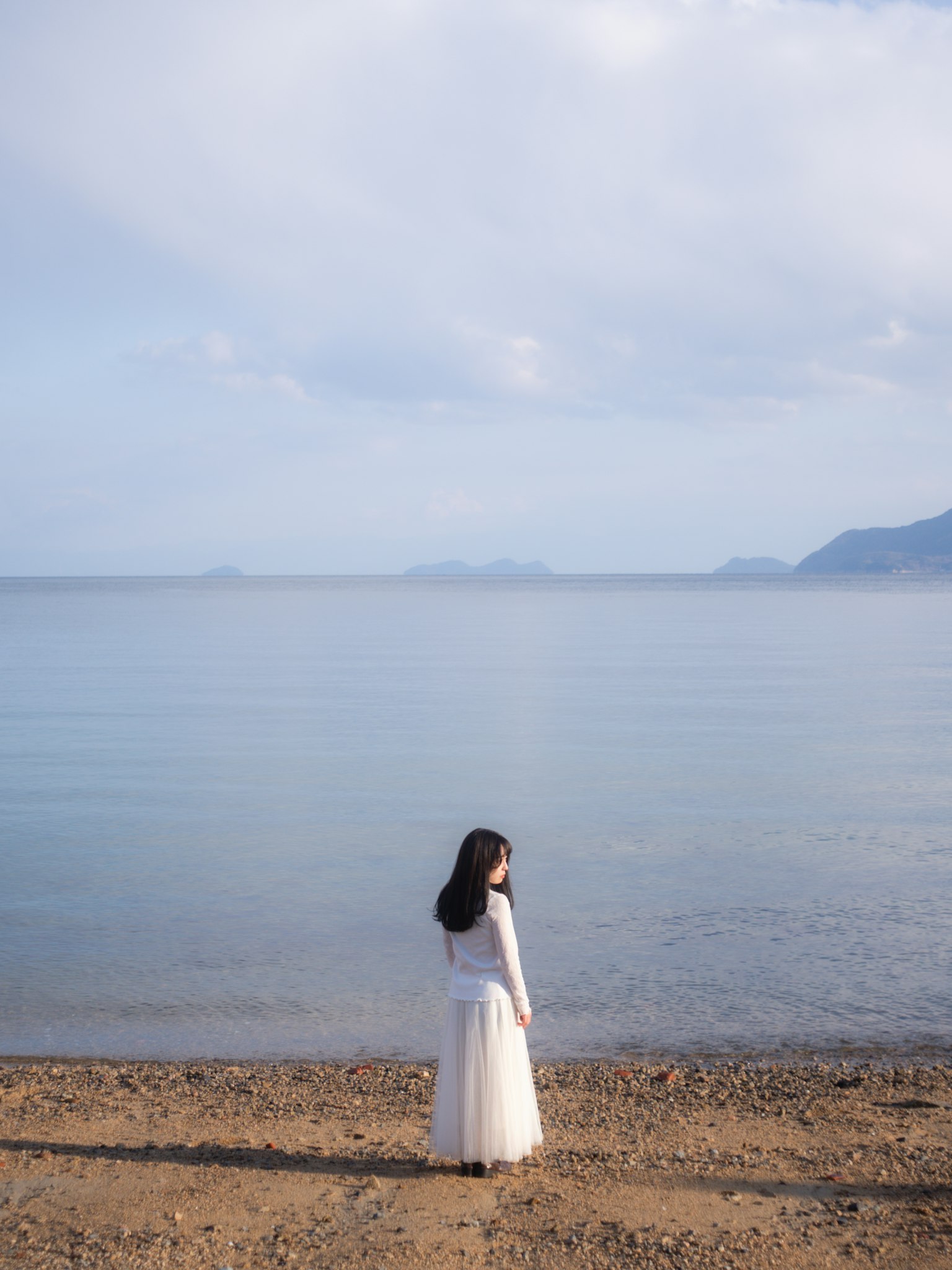 Một người phụ nữ trong chiếc đầm trắng đứng trên bãi biển yên tĩnh bên biển