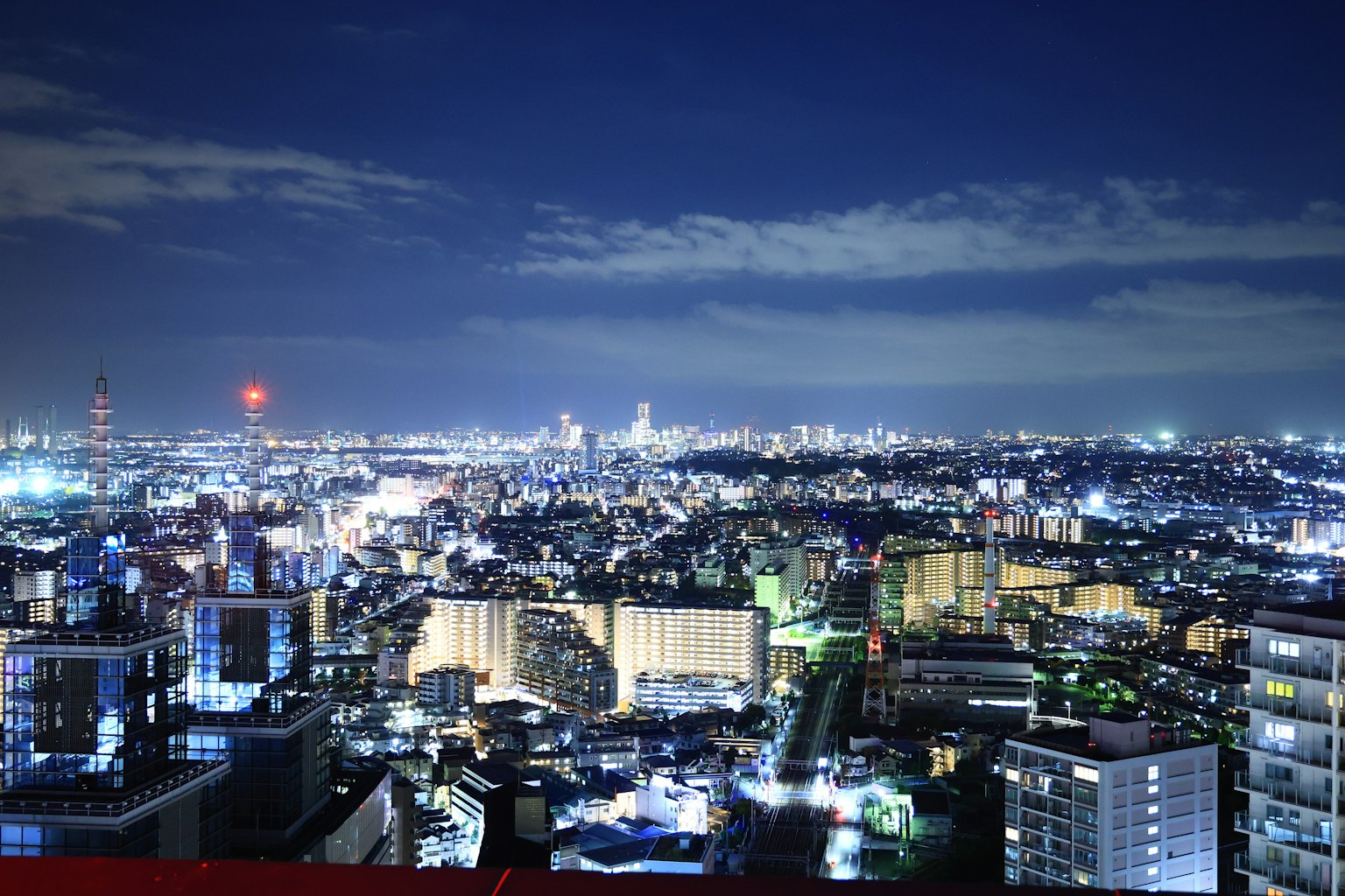 Paesaggio urbano notturno con edifici e luci brillanti, nuvole nel cielo blu
