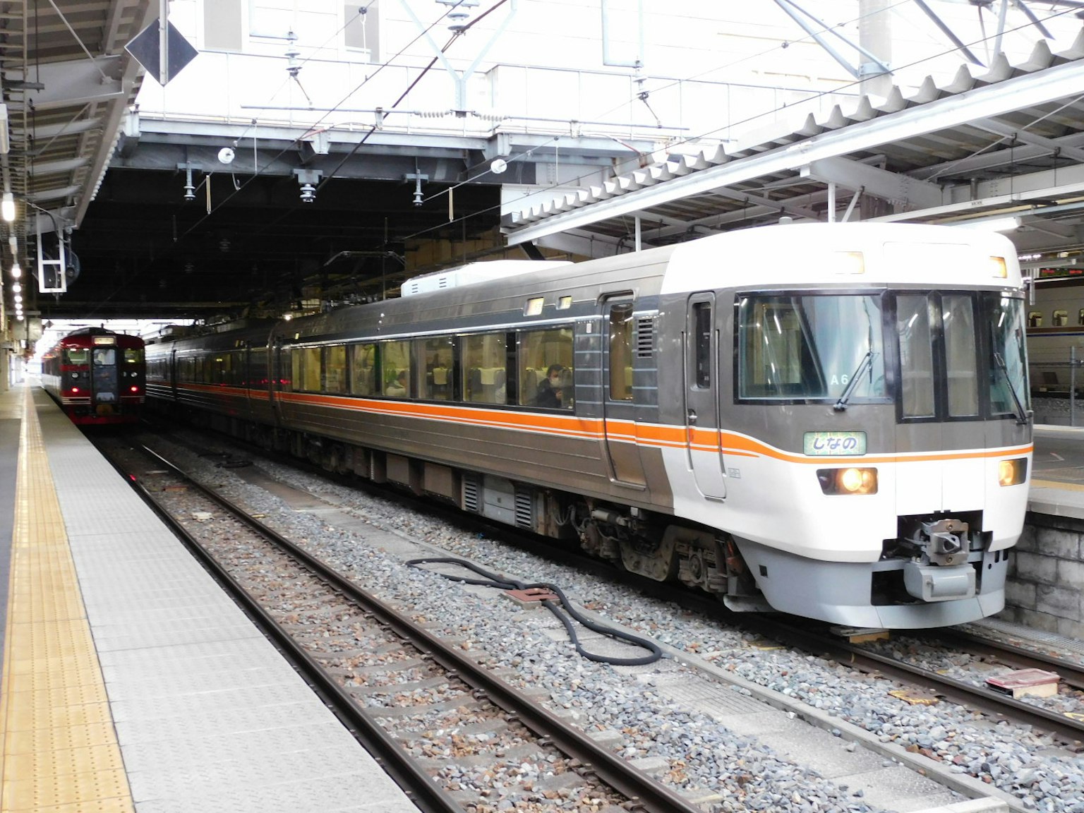 Kereta ekspres terbatas menunggu di stasiun dengan kereta lain di latar belakang