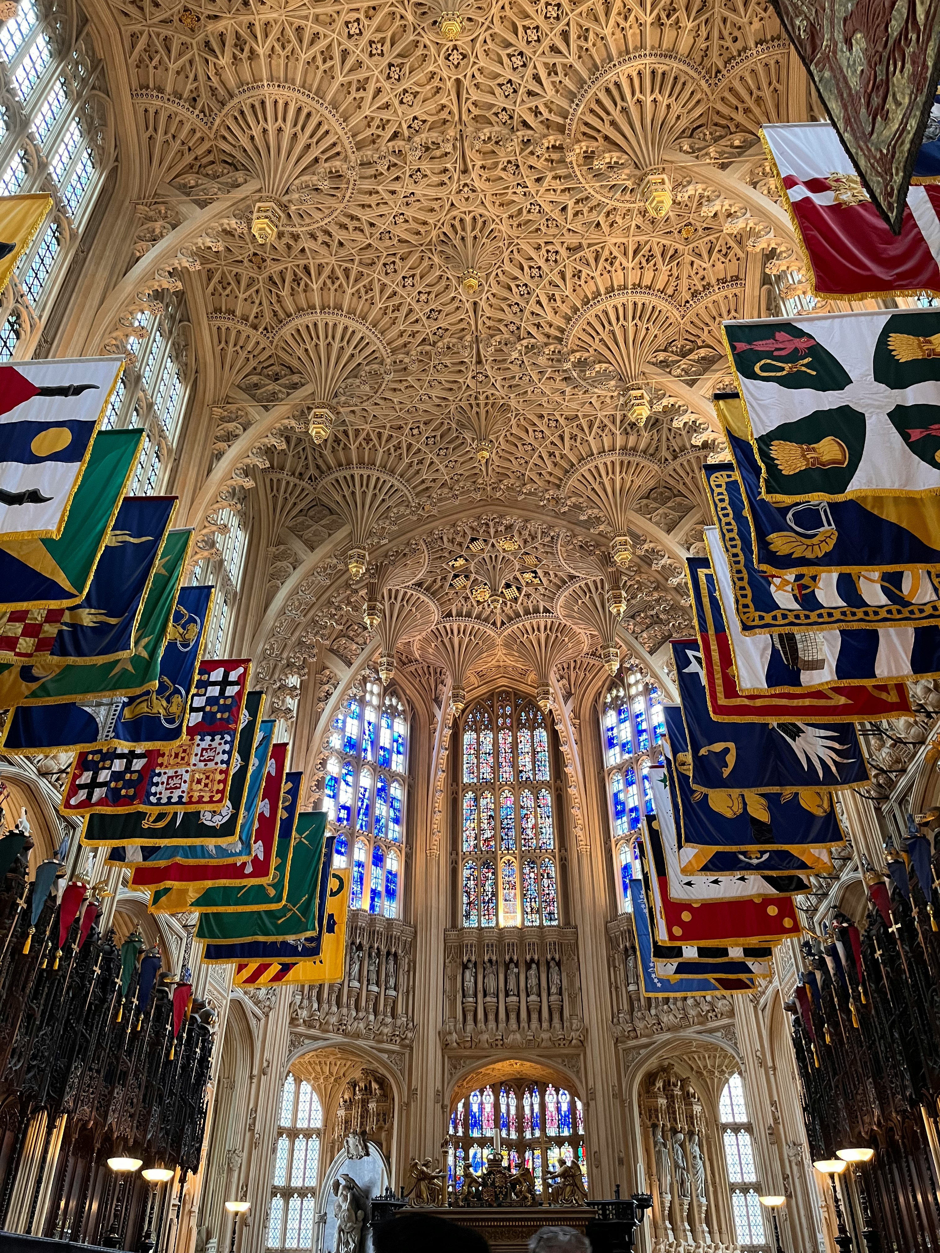 Interior de una catedral con techo abovedado alto, vitrales y estandartes colgantes