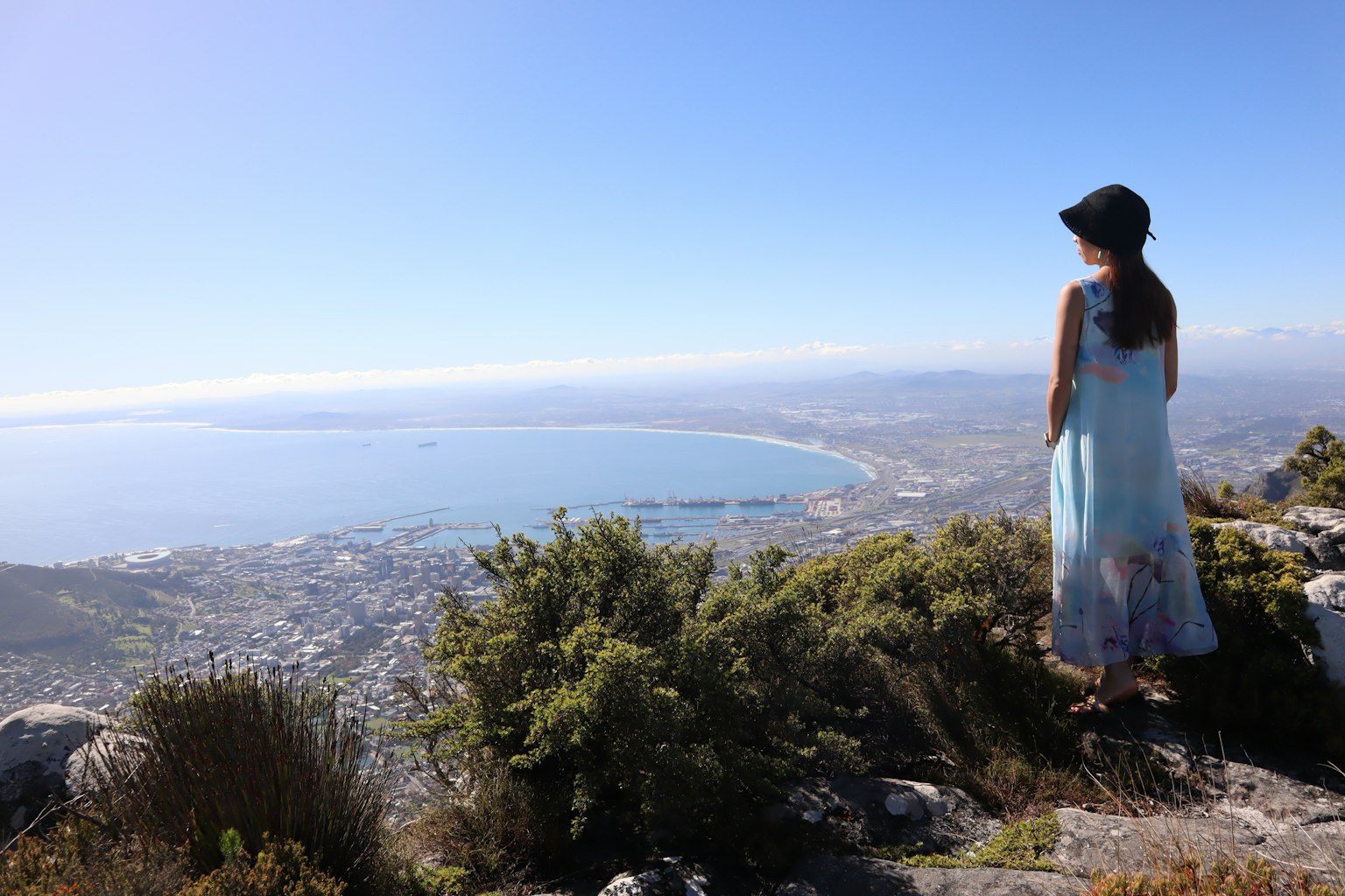 穿着蓝色连衣裙的女性在山顶俯瞰海岸风景