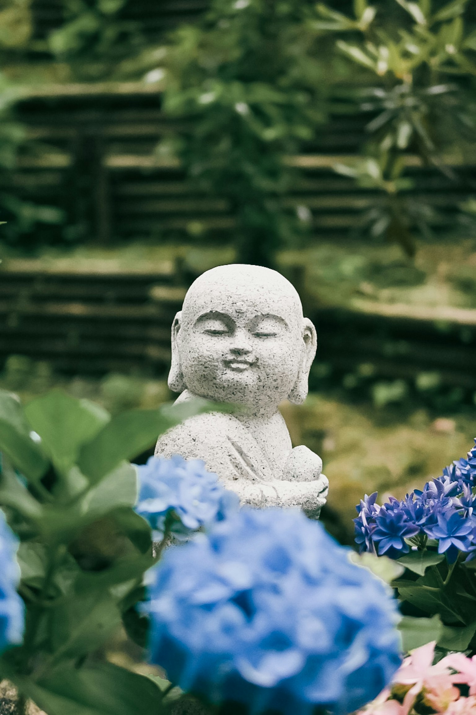Patung batu Buddha tersenyum di antara bunga biru
