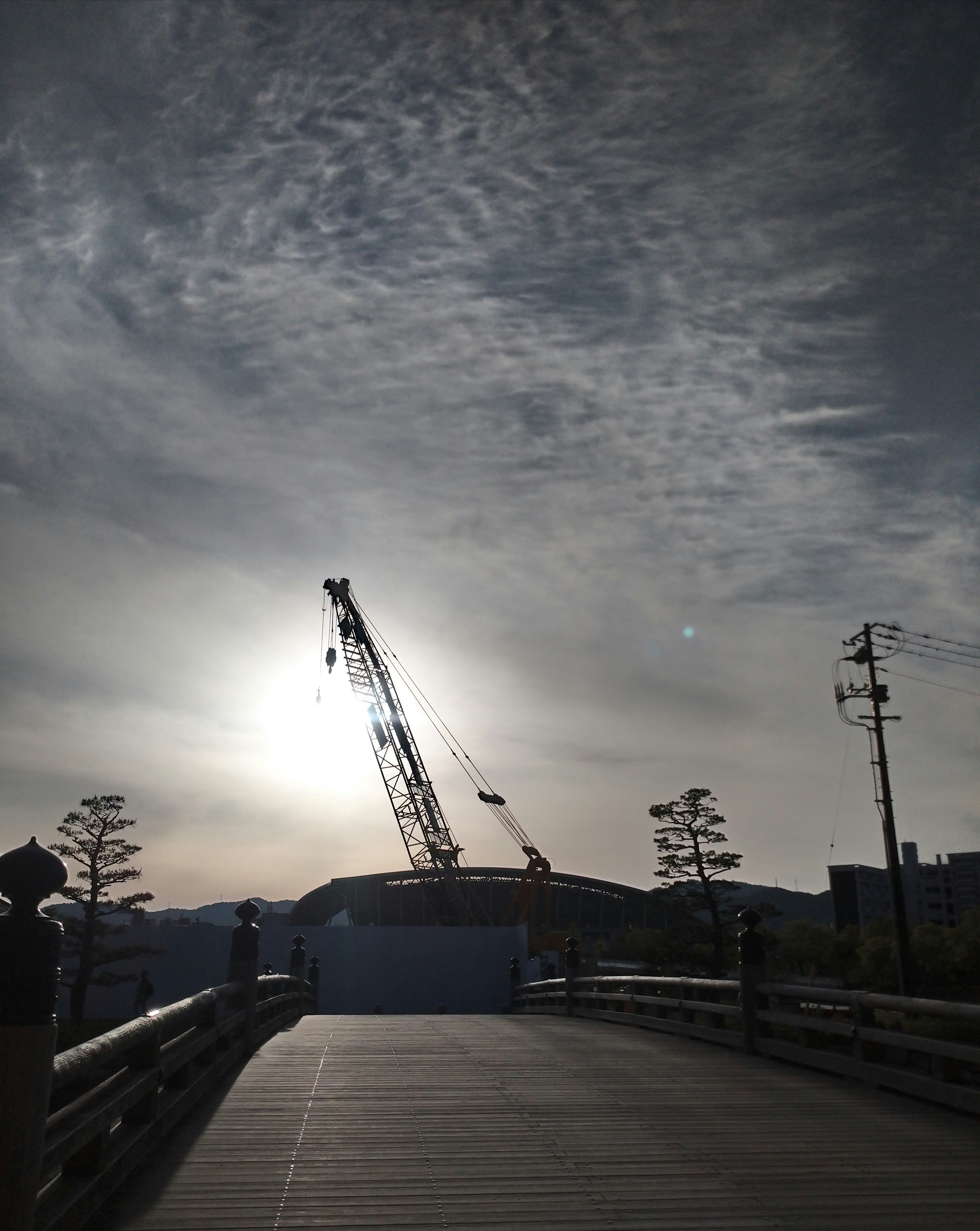 逆光の夕暮れにクレーンが立つ工事現場の歩道