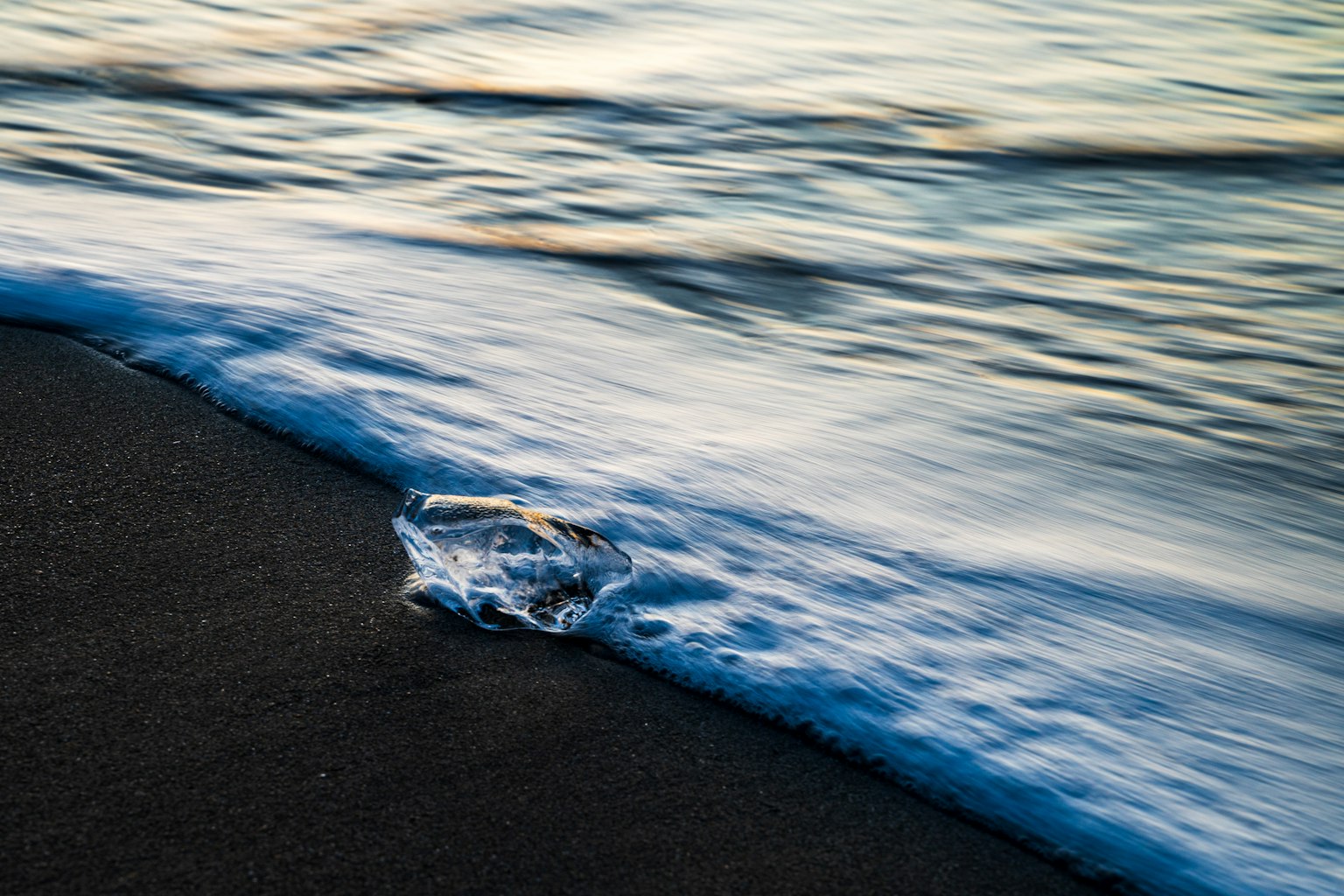 Gambar fragmen es bening di pantai berpasir dengan ombak