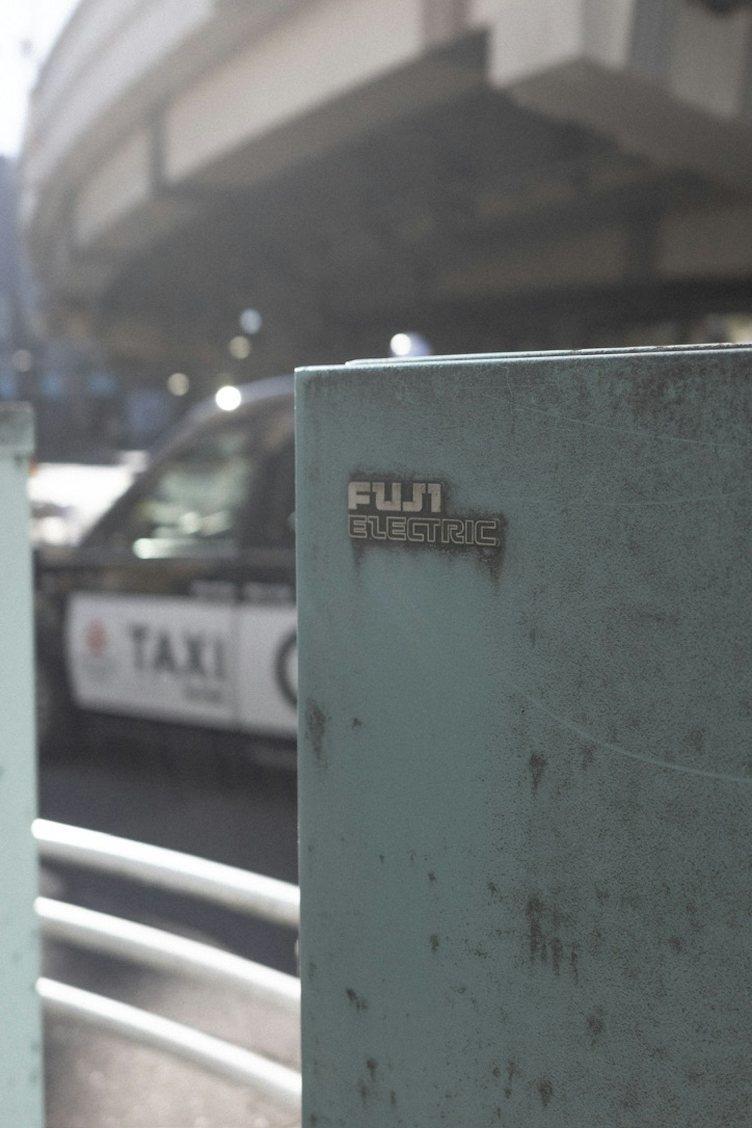 Blauer Metallpfeiler mit Fuji-Logo und einem Taxi im Hintergrund