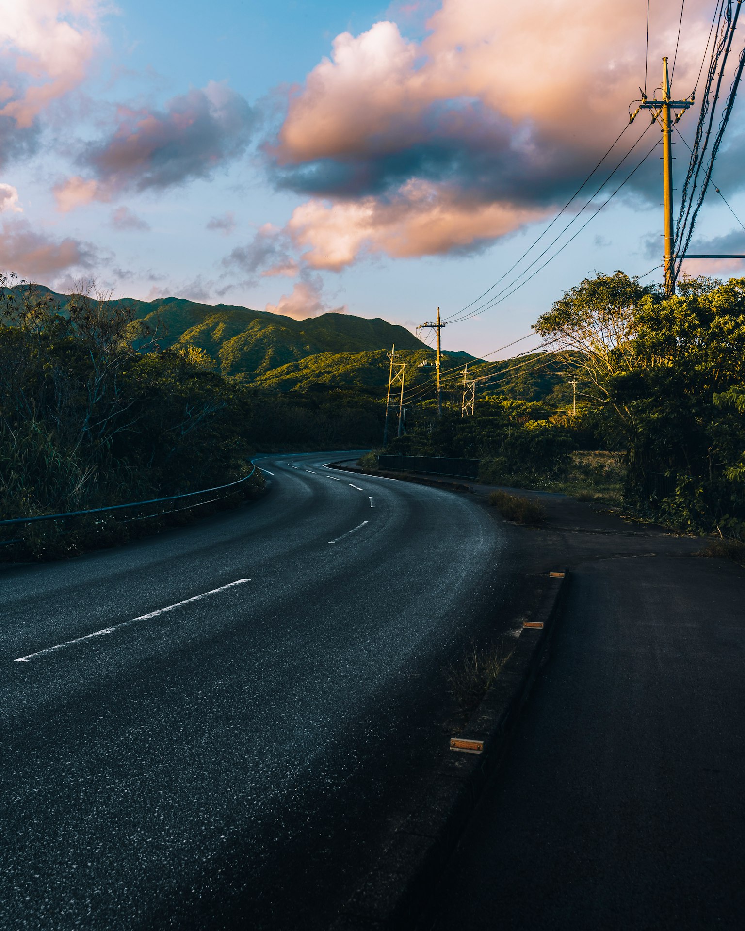 Route sinueuse le long de montagnes verdoyantes sous un ciel nuageux