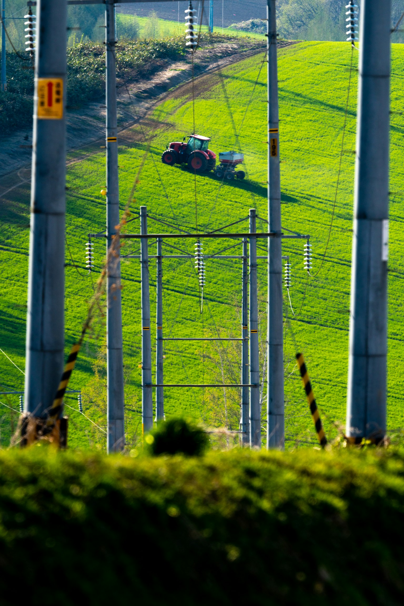 Traktor arbeitet auf einem grünen Hügel mit Strommasten im Vordergrund