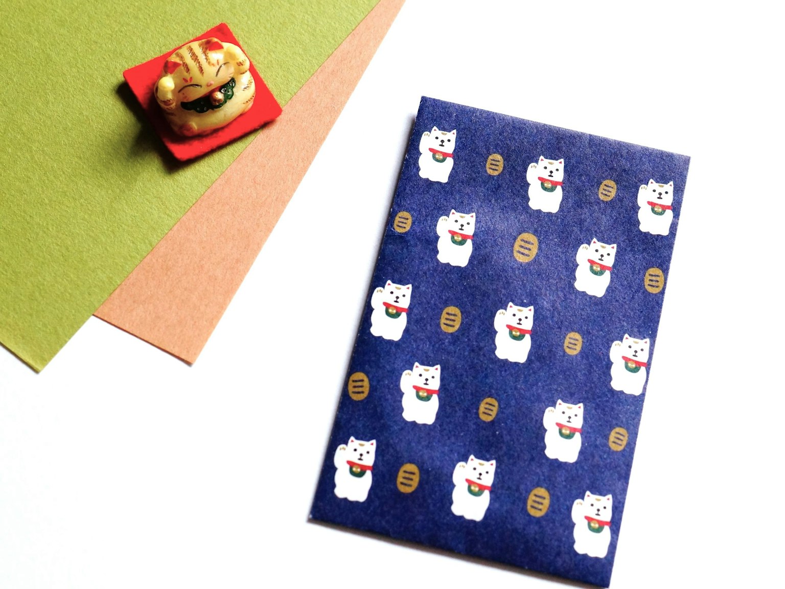 Sebuah buku catatan dengan desain kucing di latar belakang biru disertai dengan makanan manis tradisional