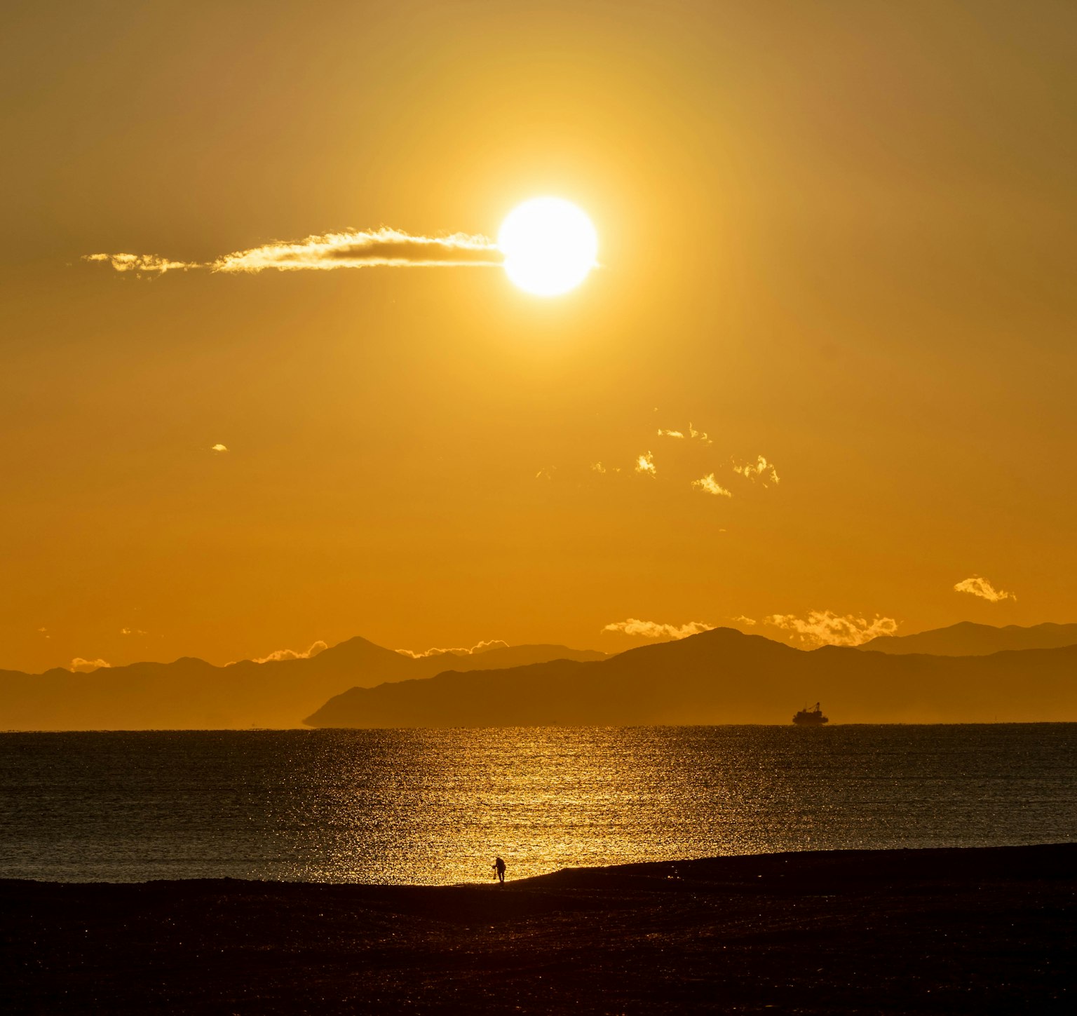 Beautiful sunset over the ocean with distant mountains and a ship