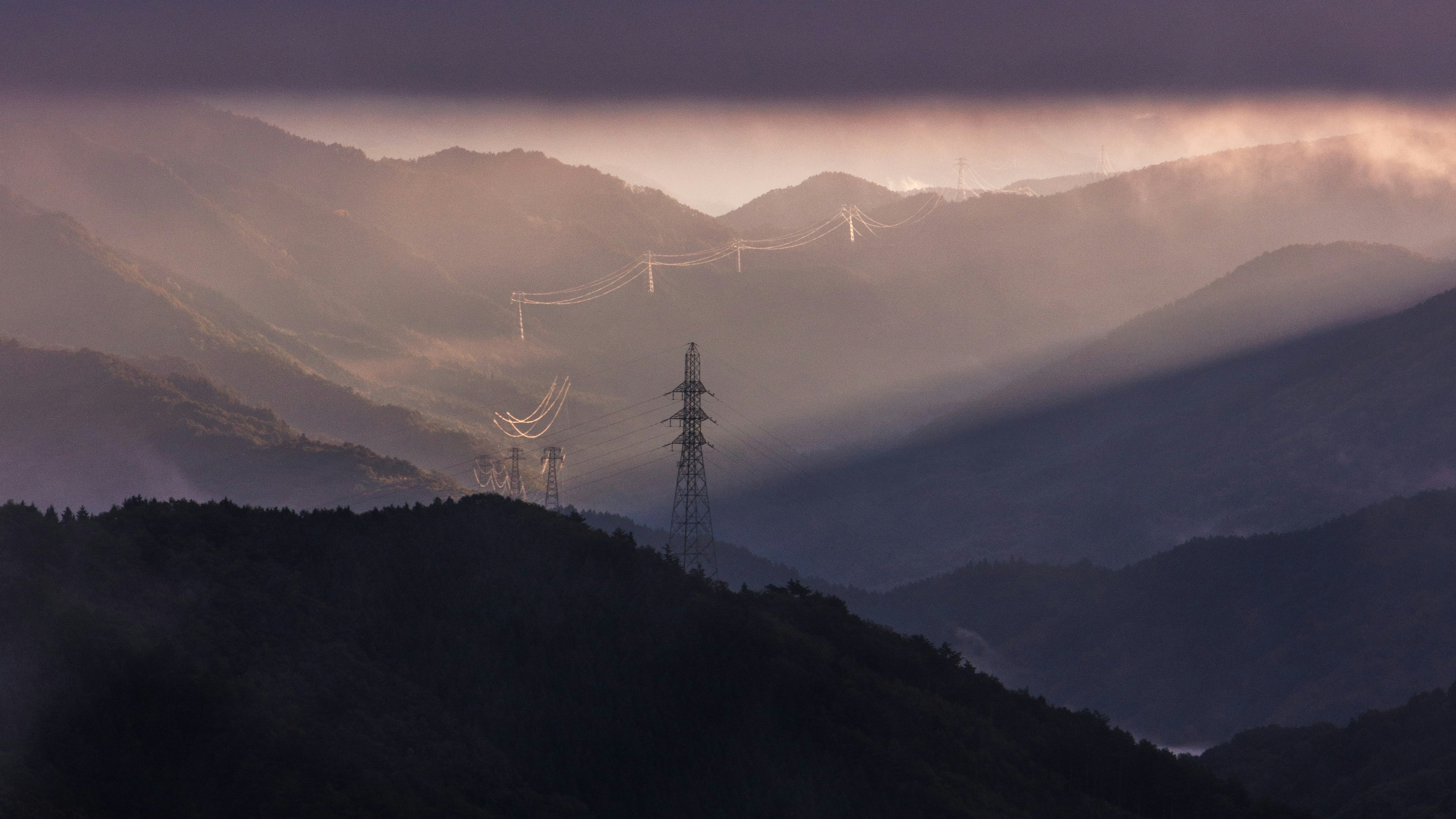 霧に包まれた山並みと送電鉄塔のある風景