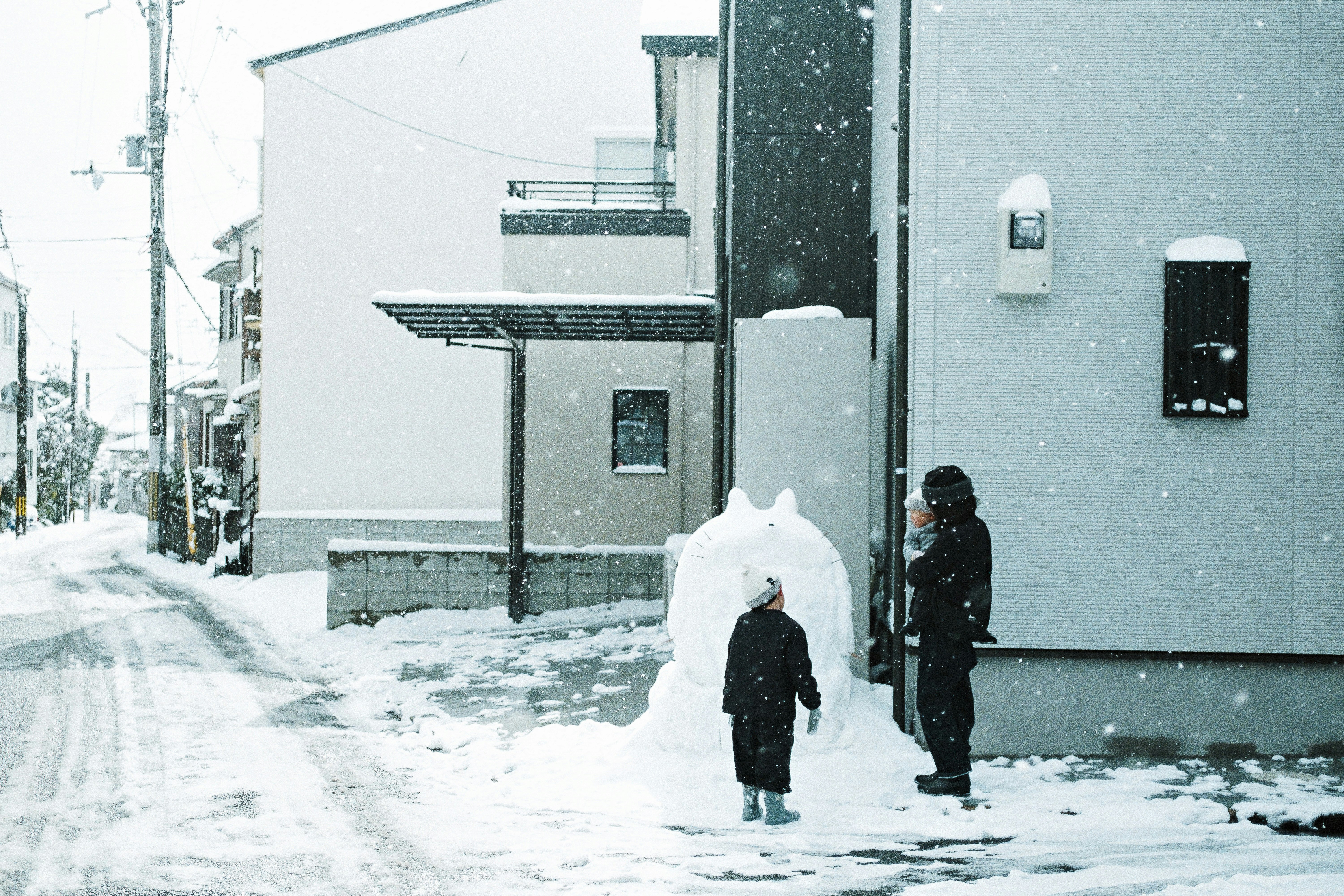 雪の降る住宅街で歩く人々の後ろ姿