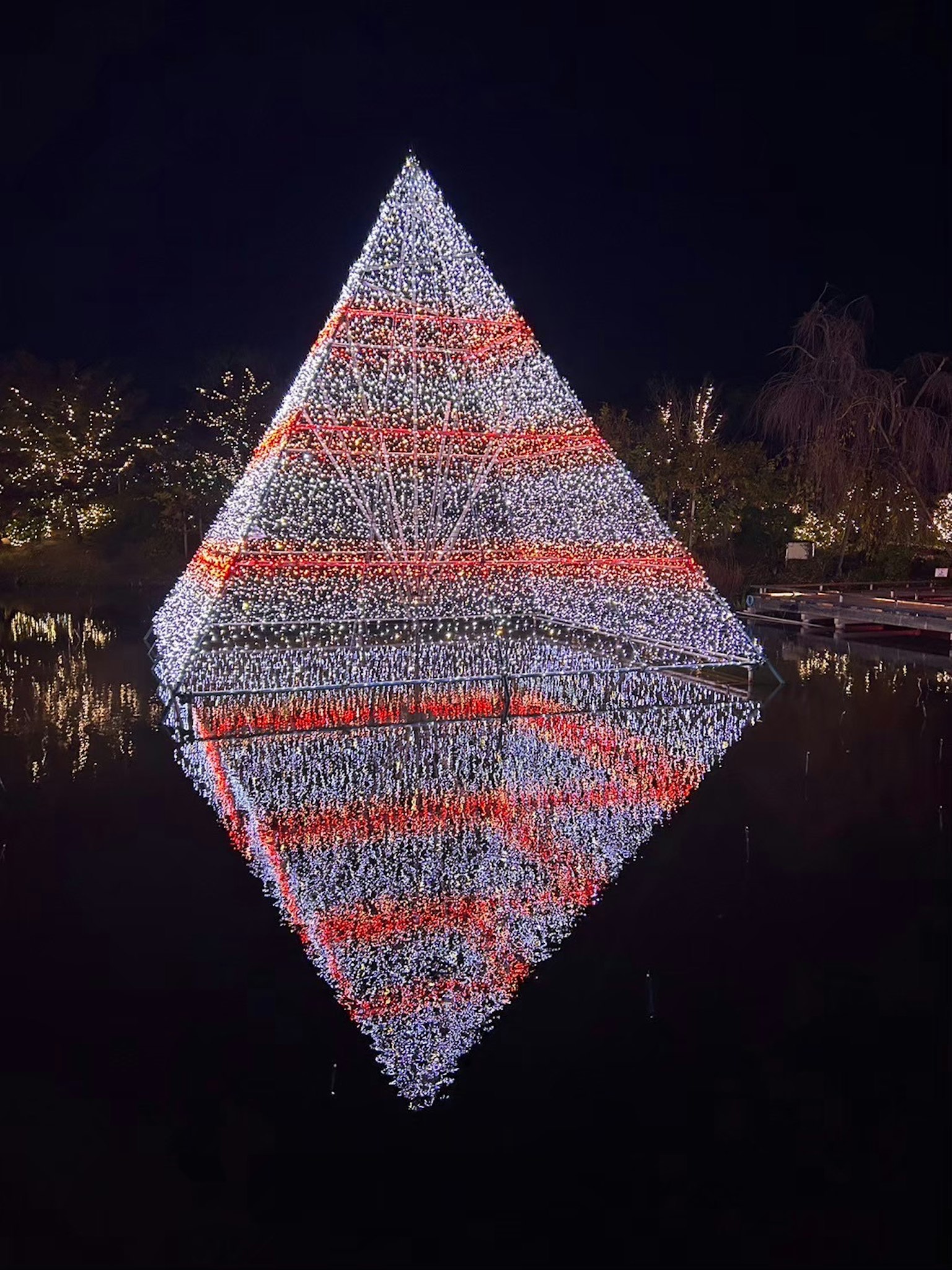 Pirámide iluminada con luces naranjas y blancas reflejándose en el agua por la noche