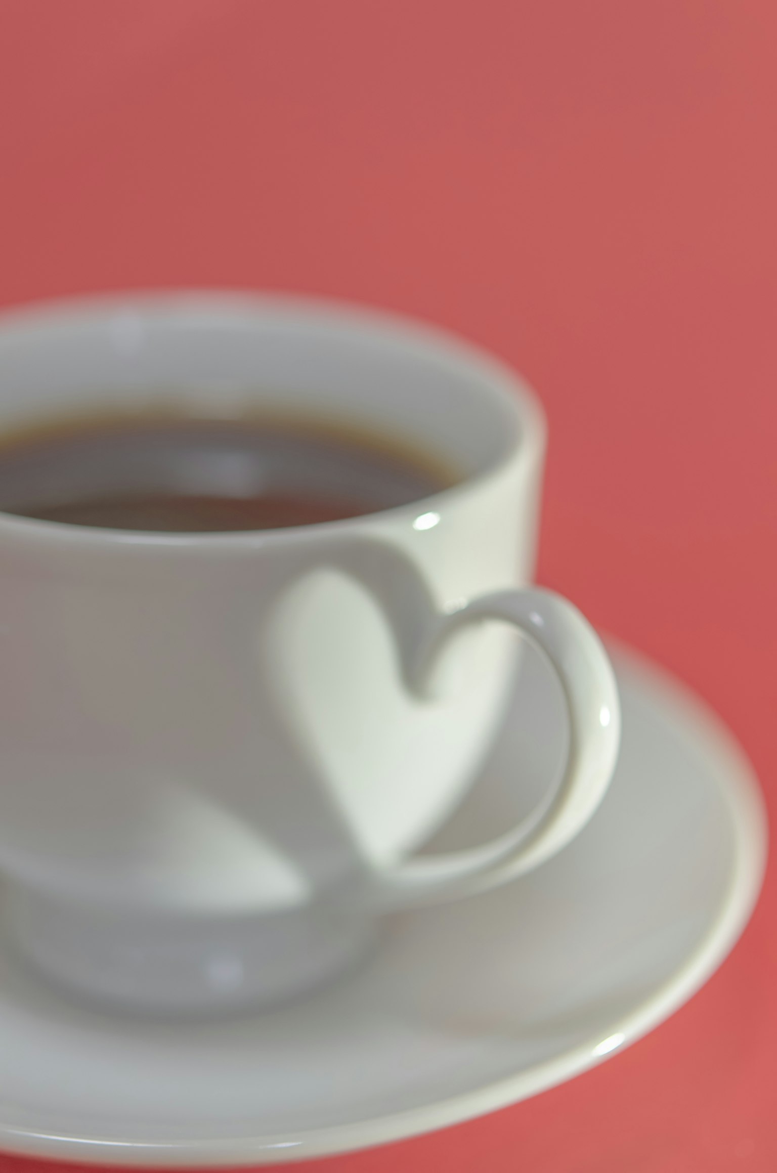 Tazza da caffè bianca con manico a forma di cuore su sfondo rosa