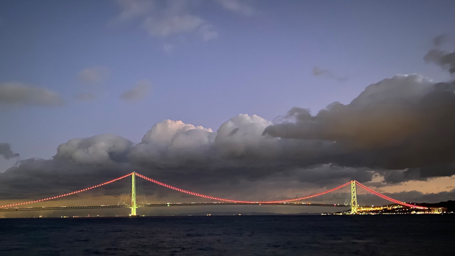 Scenic view of a bridge illuminated at dusk with red cables and bright lights