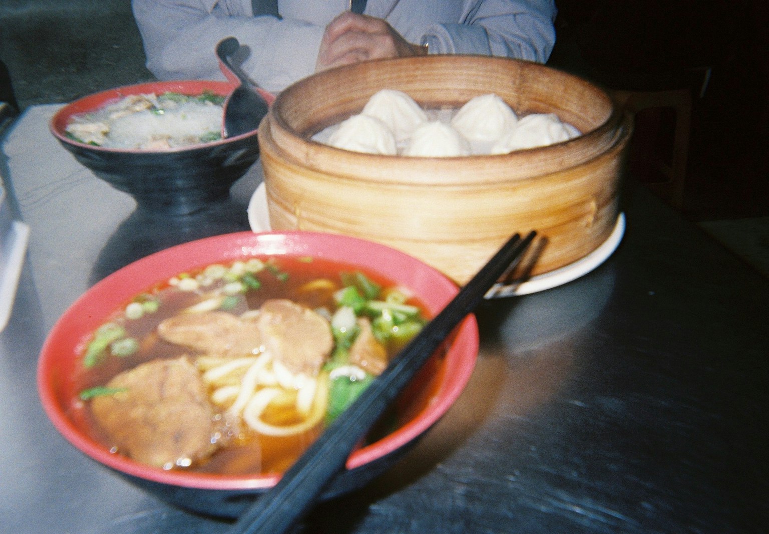 A red bowl with ramen featuring slices of meat and green vegetables