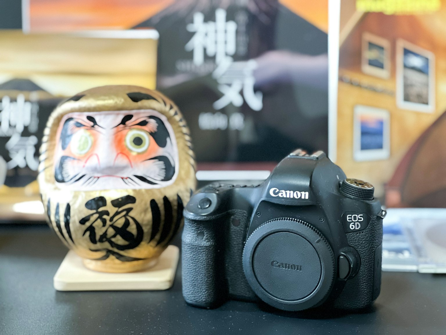 A Canon camera next to a Daruma doll on a table with colorful backgrounds