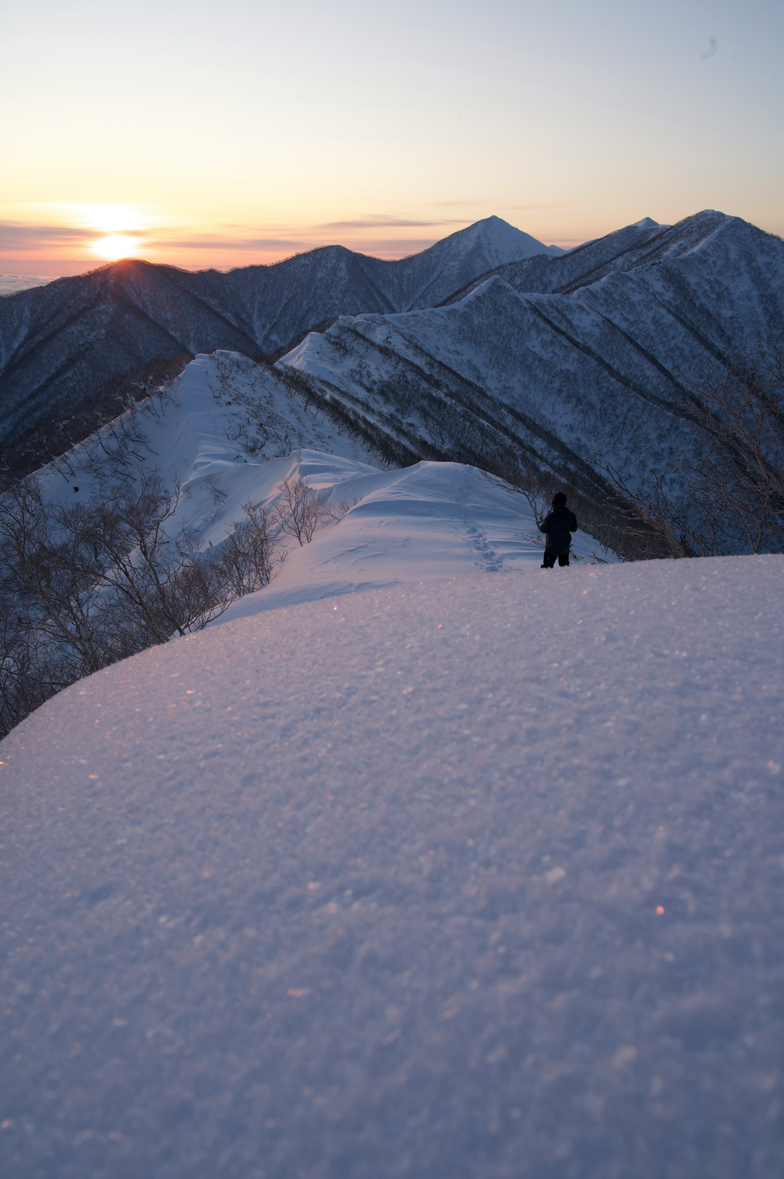 Silueta de un excursionista en una cresta montañosa cubierta de nieve con un atardecer de fondo