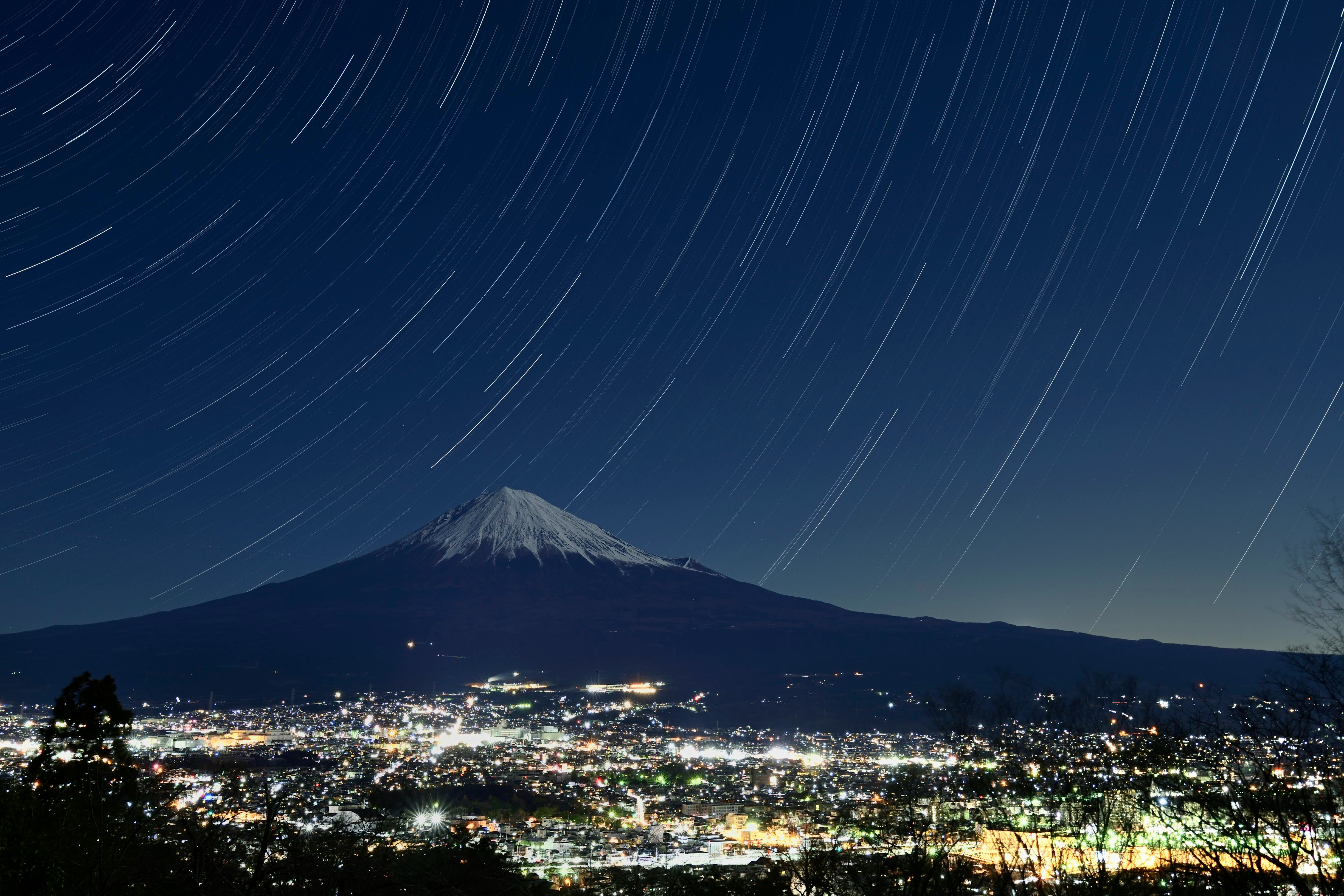 夜景の街と星の軌跡、遠くにそびえる山