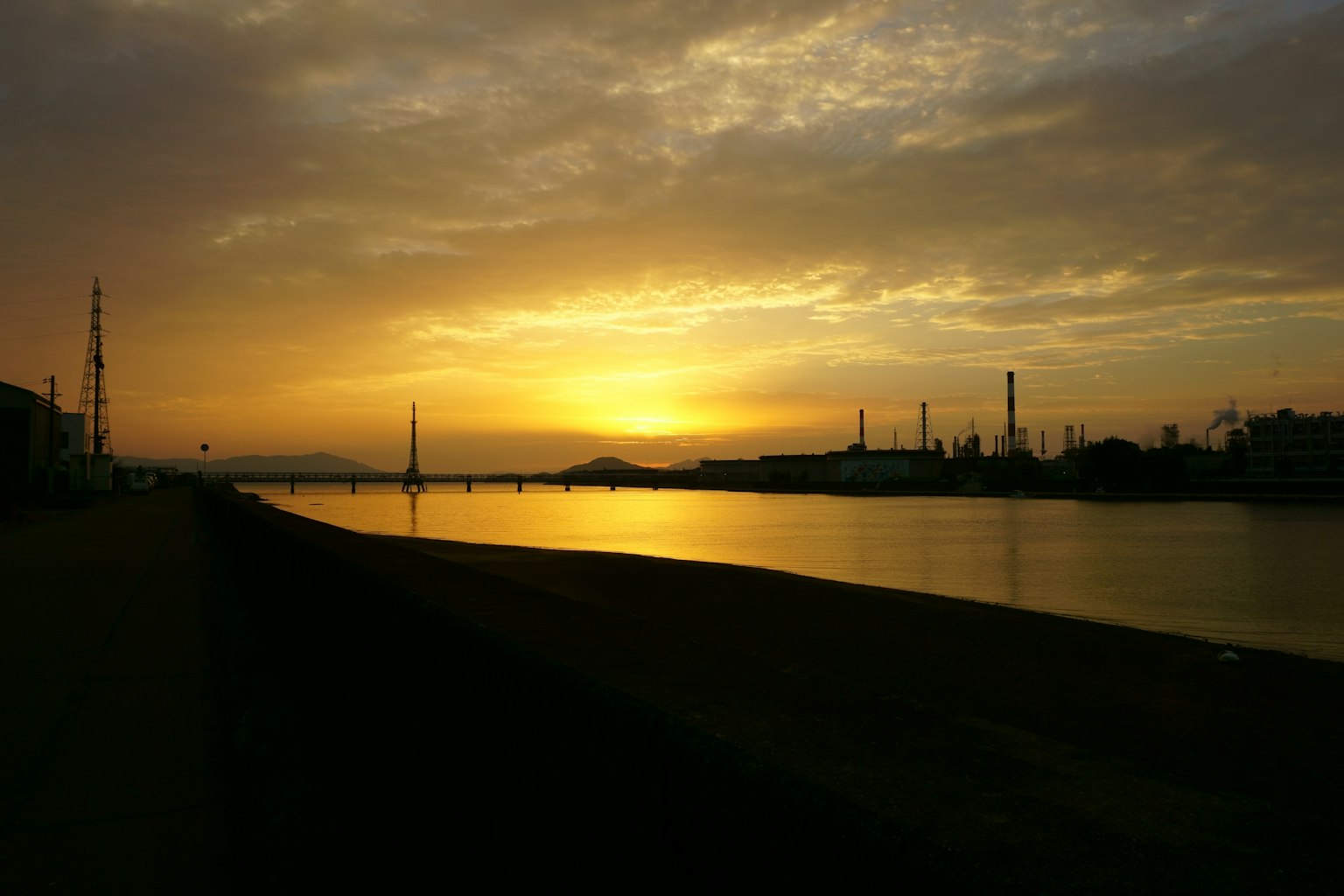 Malersicher Flussblick bei Sonnenuntergang mit industriellen Silhouetten im Hintergrund