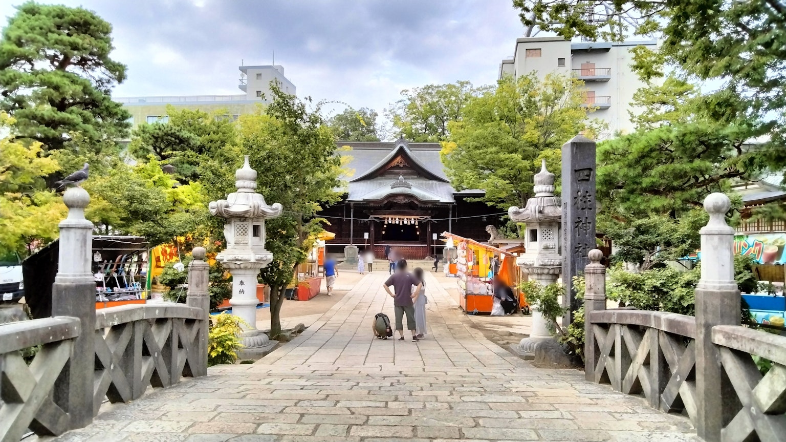 People walking across a stone bridge towards a shrine surrounded by lush greenery and stone lanterns